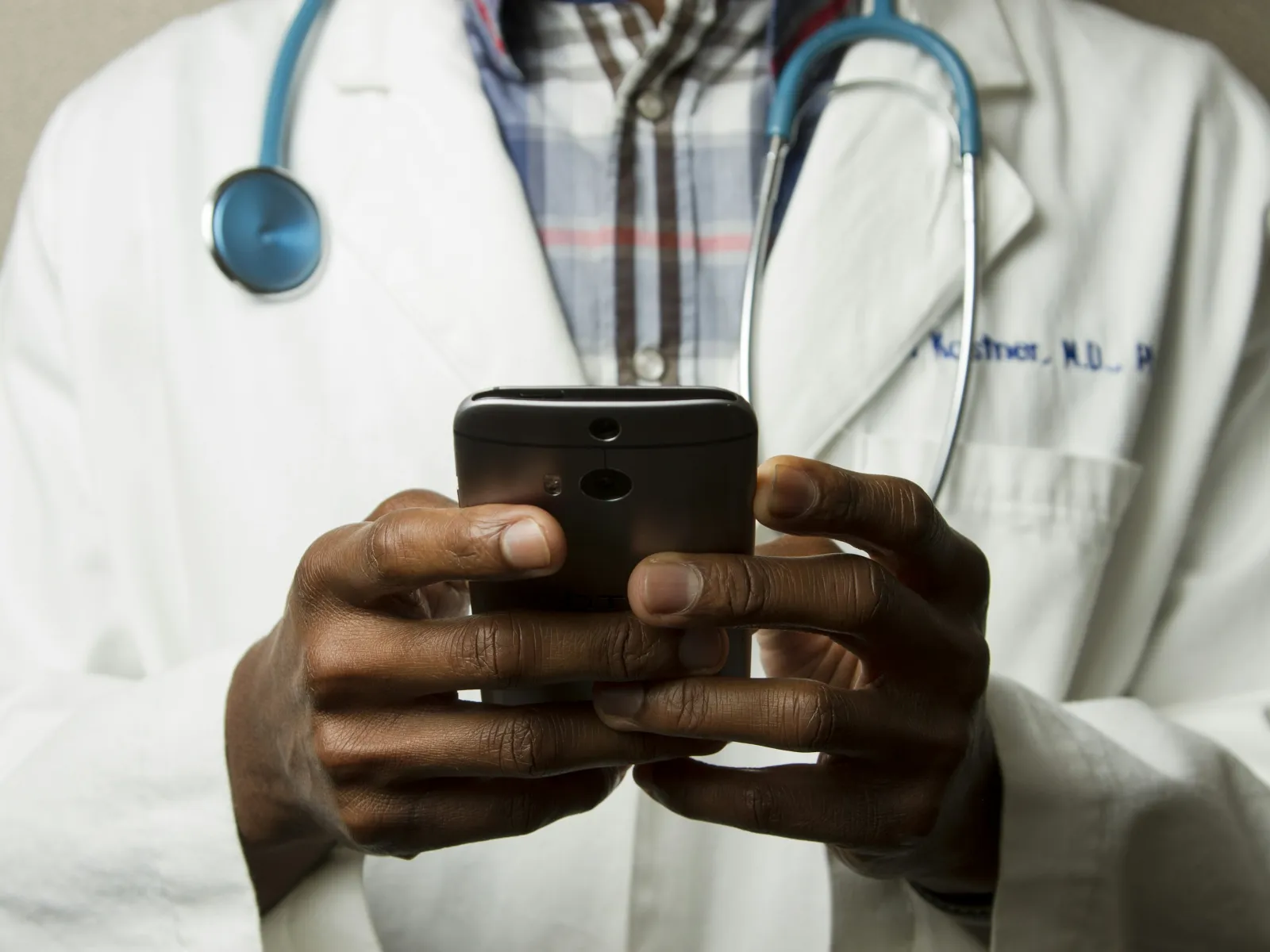 Close-up of a doctor in white coat using a smartphone with a stethoscope around the neck