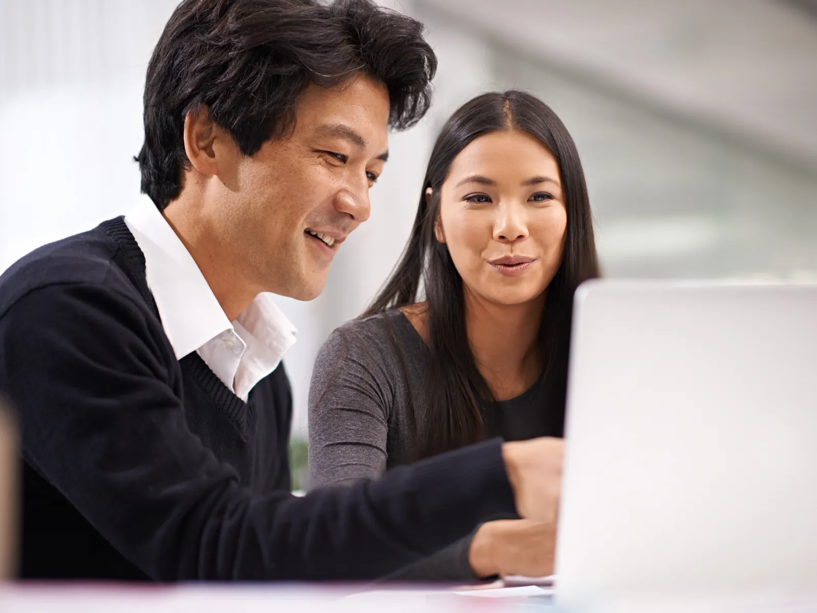 Two colleagues smiling and discussing work while looking at a laptop screen in an office setting