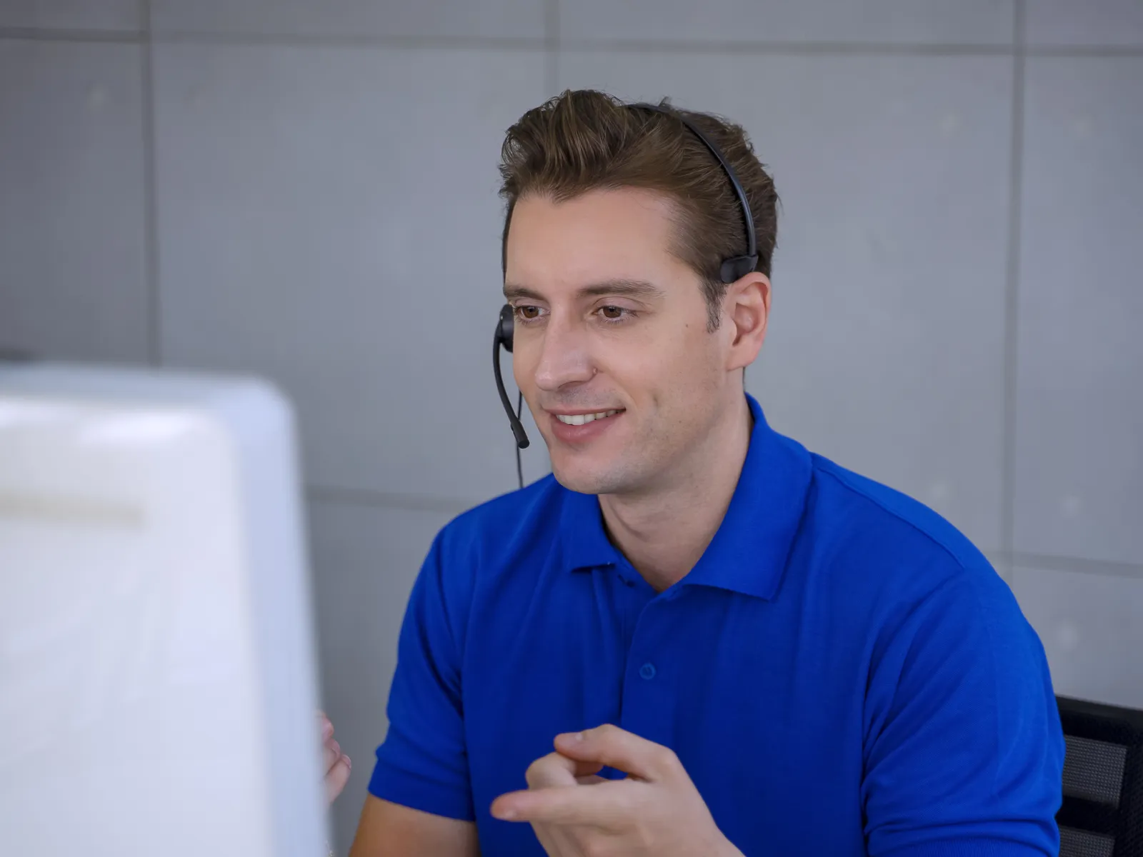 Man in blue polo shirt wearing headset working at computer, engaged in customer support or remote communication.