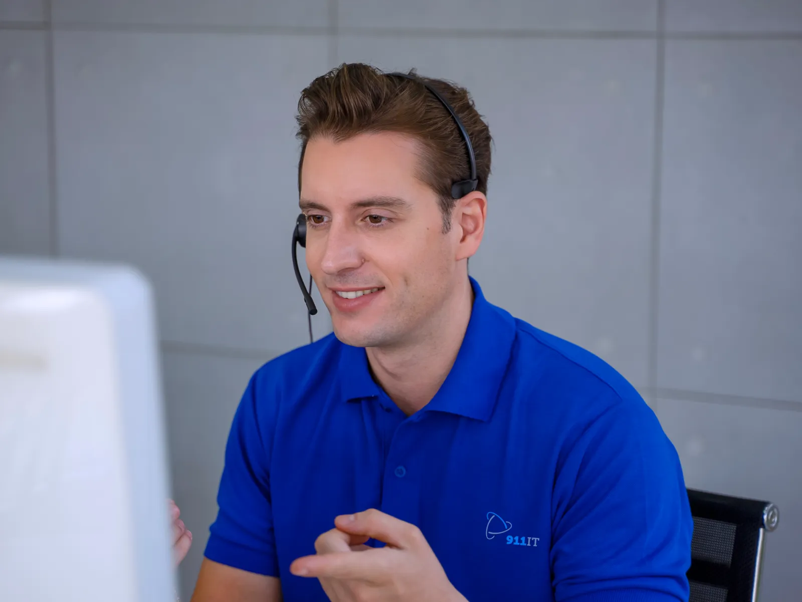Customer service representative wearing headset and blue 911IT polo shirt assisting a client via computer.