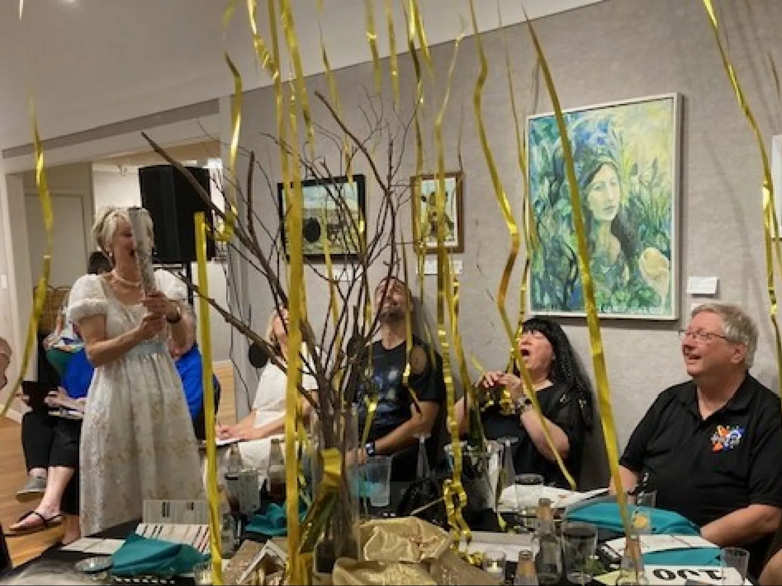 People enjoying a celebration with gold streamers and artwork displayed on gallery walls