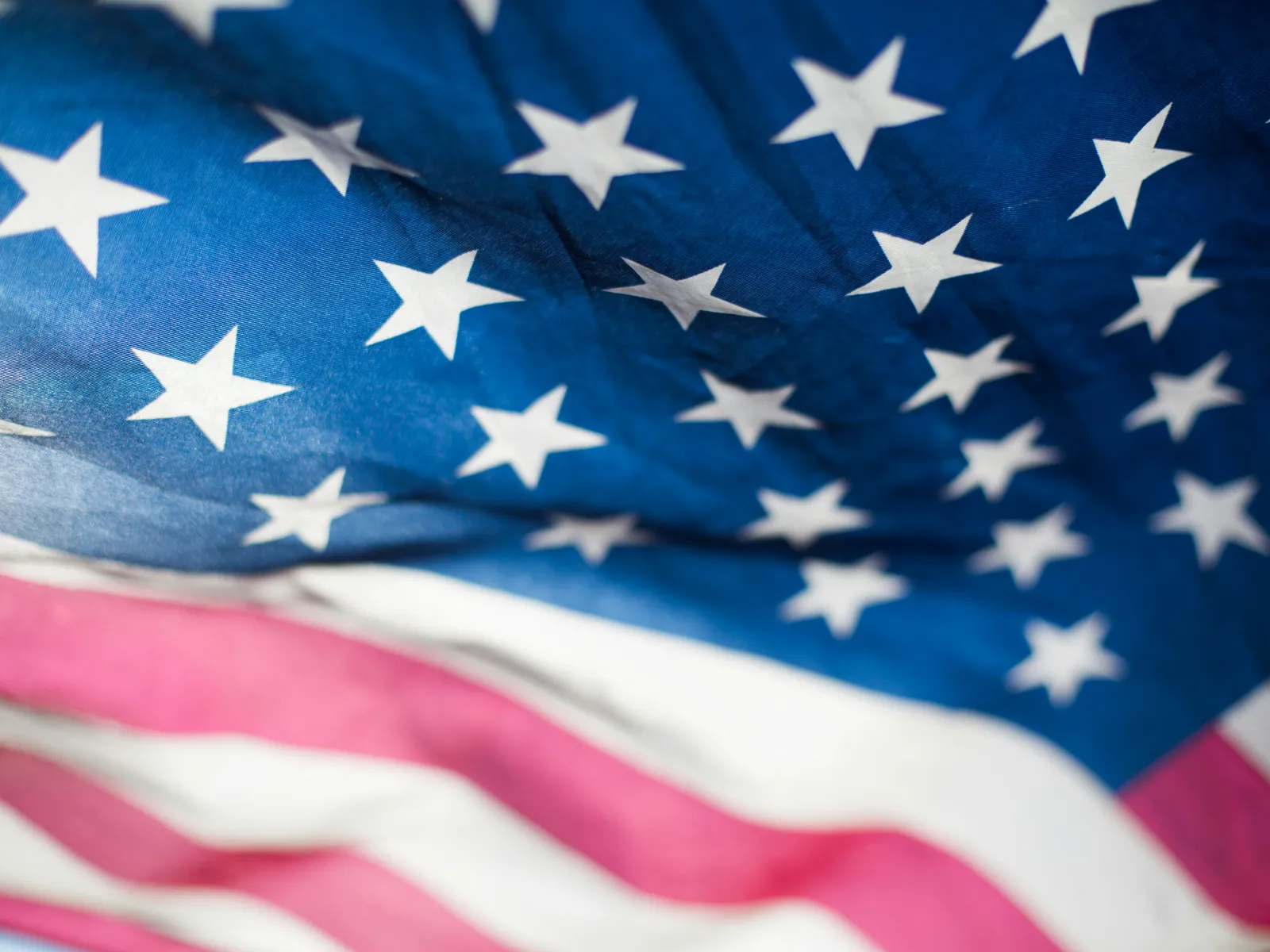 Close-up of the American flag showing white stars on blue background and red and white stripes in soft focus.