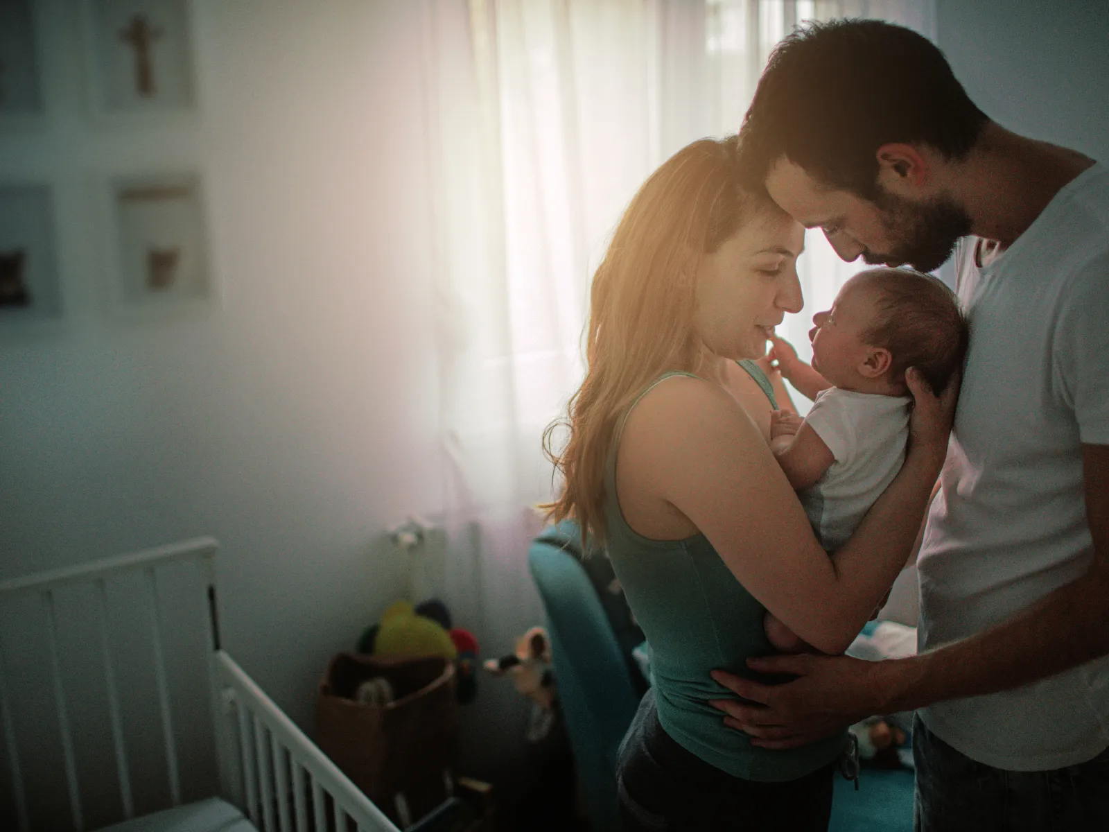 New parents lovingly hold their newborn in a cozy nursery filled with soft light.
