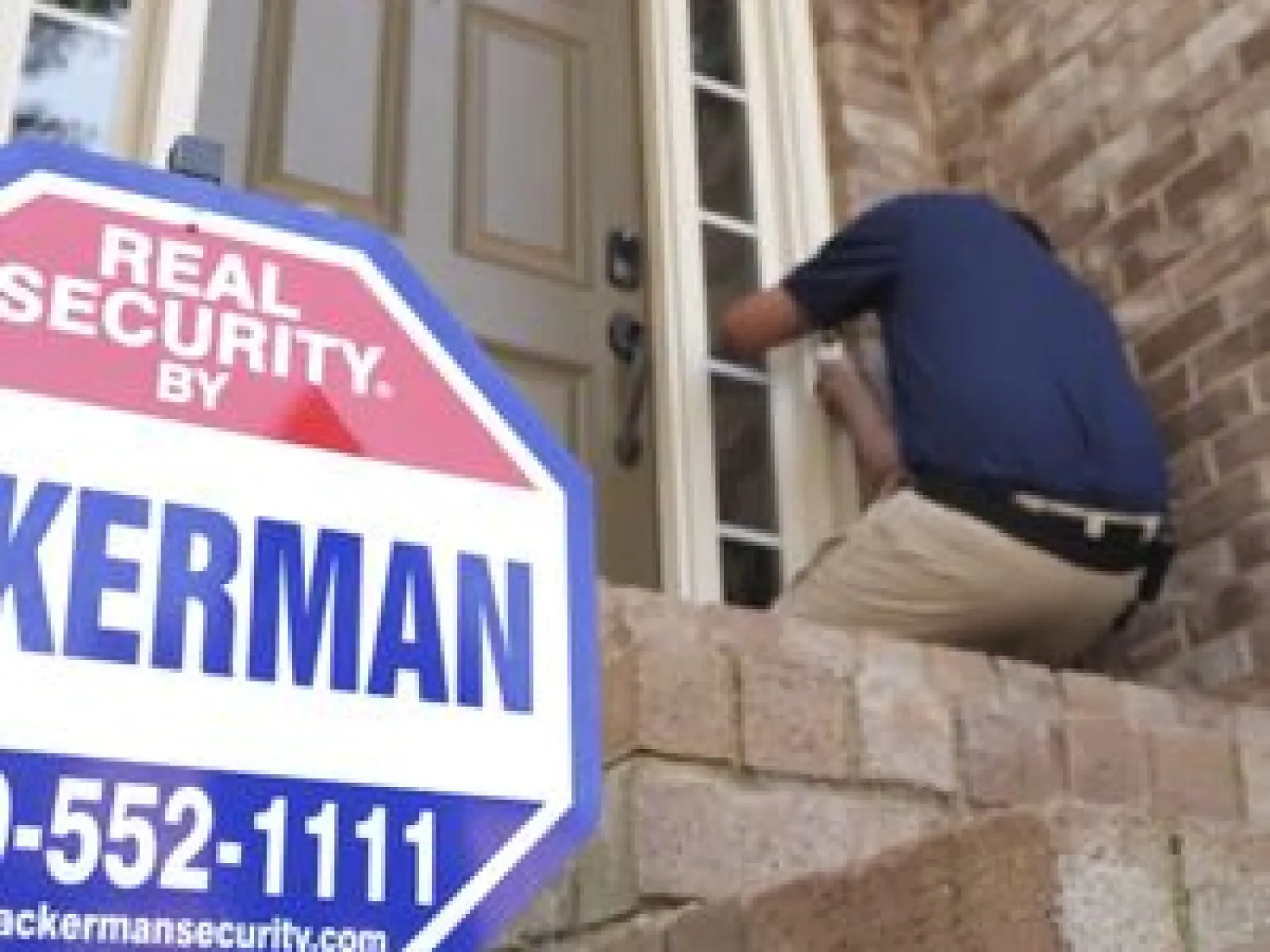 Security professional installing or inspecting a lock on a residential front door with a Kerman security sign in foreground