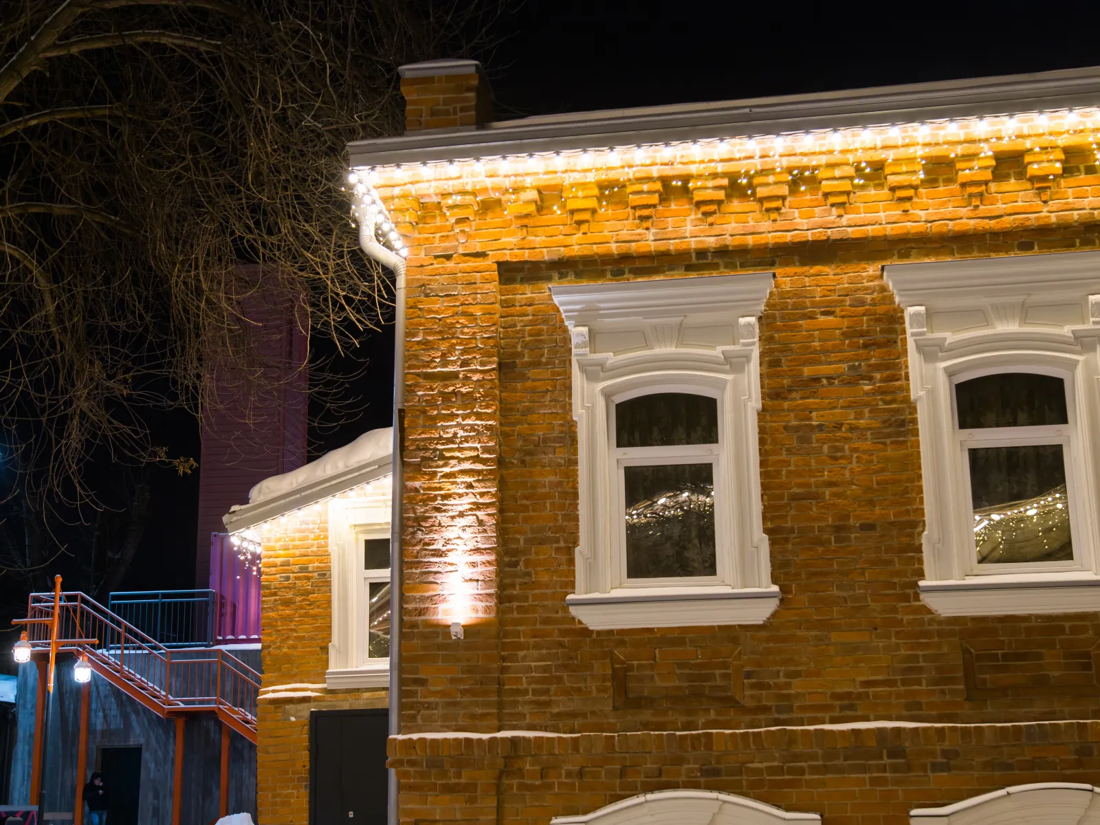 Historic brick building illuminated at night with white window frames and string lights on the roofline.