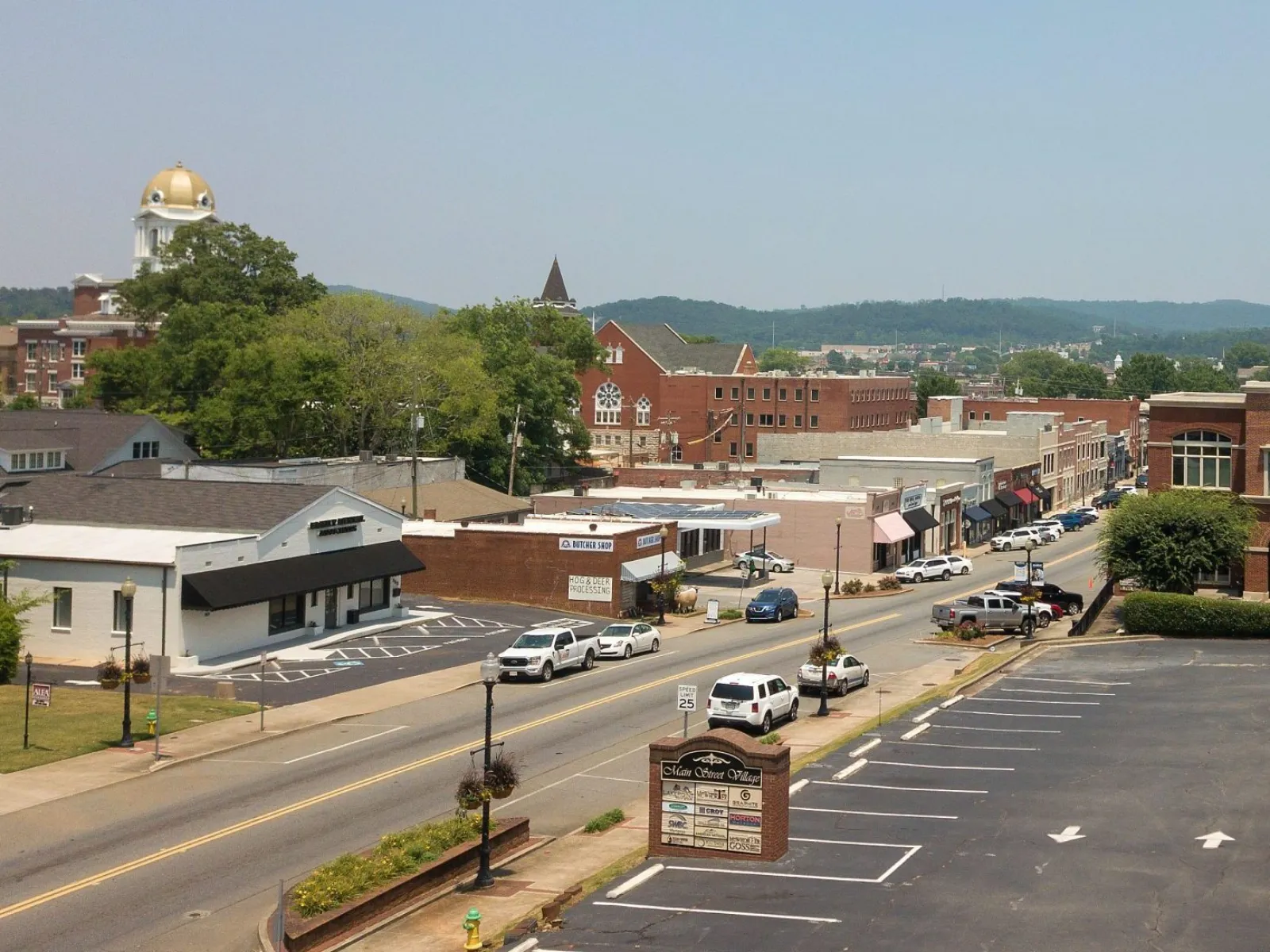 Small town main street with historic buildings, parked cars, and a gold-domed courthouse in the background under clear sky.