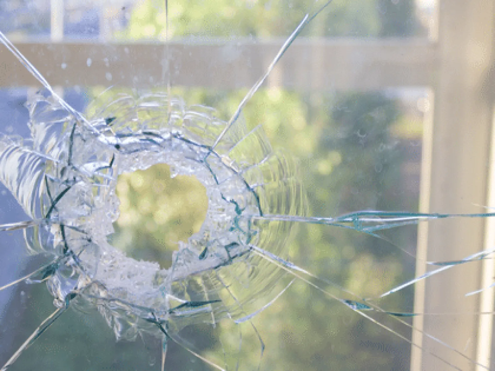Close-up of a shattered glass window with a bullet hole and visible cracks spreading outward.