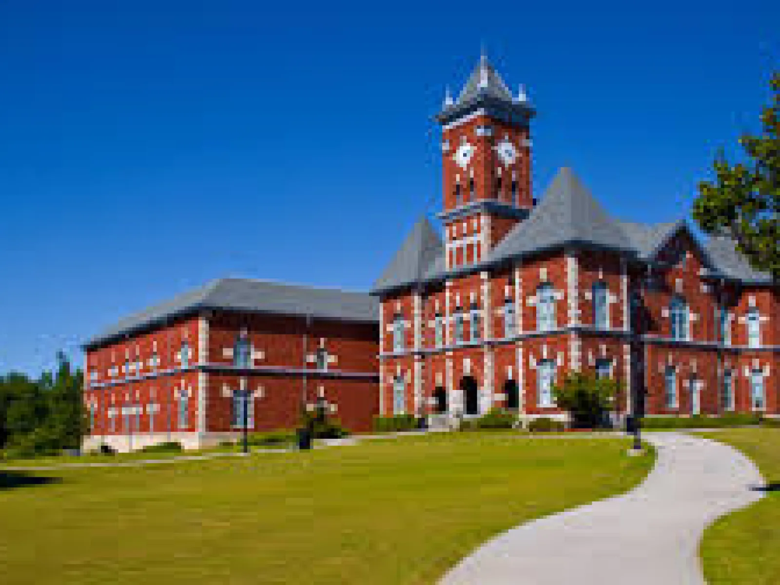 Historic red brick building with a clock tower set in green lawn under clear blue sky