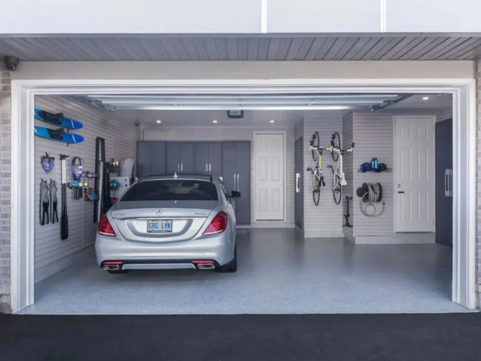 Neatly organized garage with a silver car, bicycles, ski gear, and storage cabinets in a clean space.