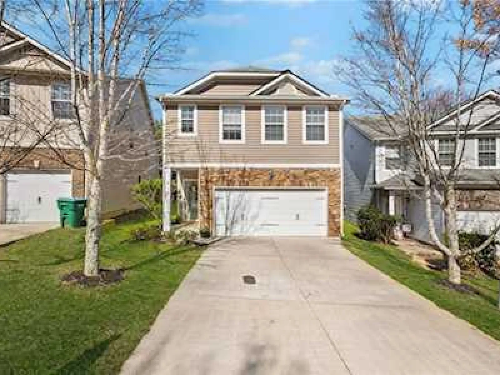 Two-story suburban house in Lawrenceville, GA with two-car garage, beige siding, and a concrete driveway on a sunny day