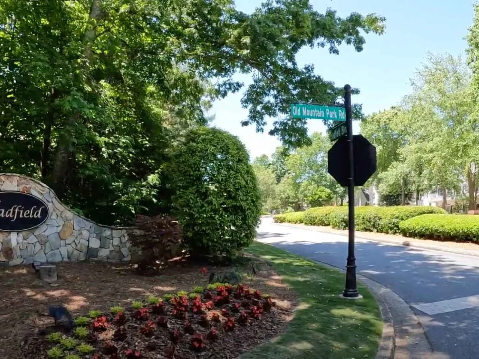 Residential neighborhood entrance with Hadfield stone sign, flowerbed, and Old Mountain Park Road street sign on sunny day.