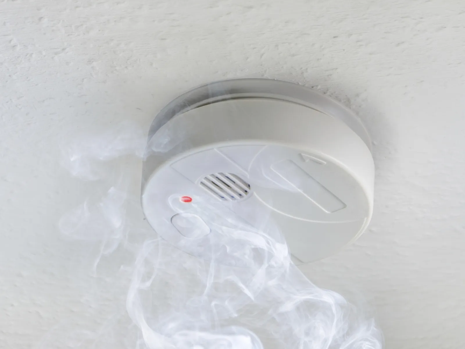 Woman cooking in kitchen with modern smoke detector mounted on wall for safety and fire prevention.