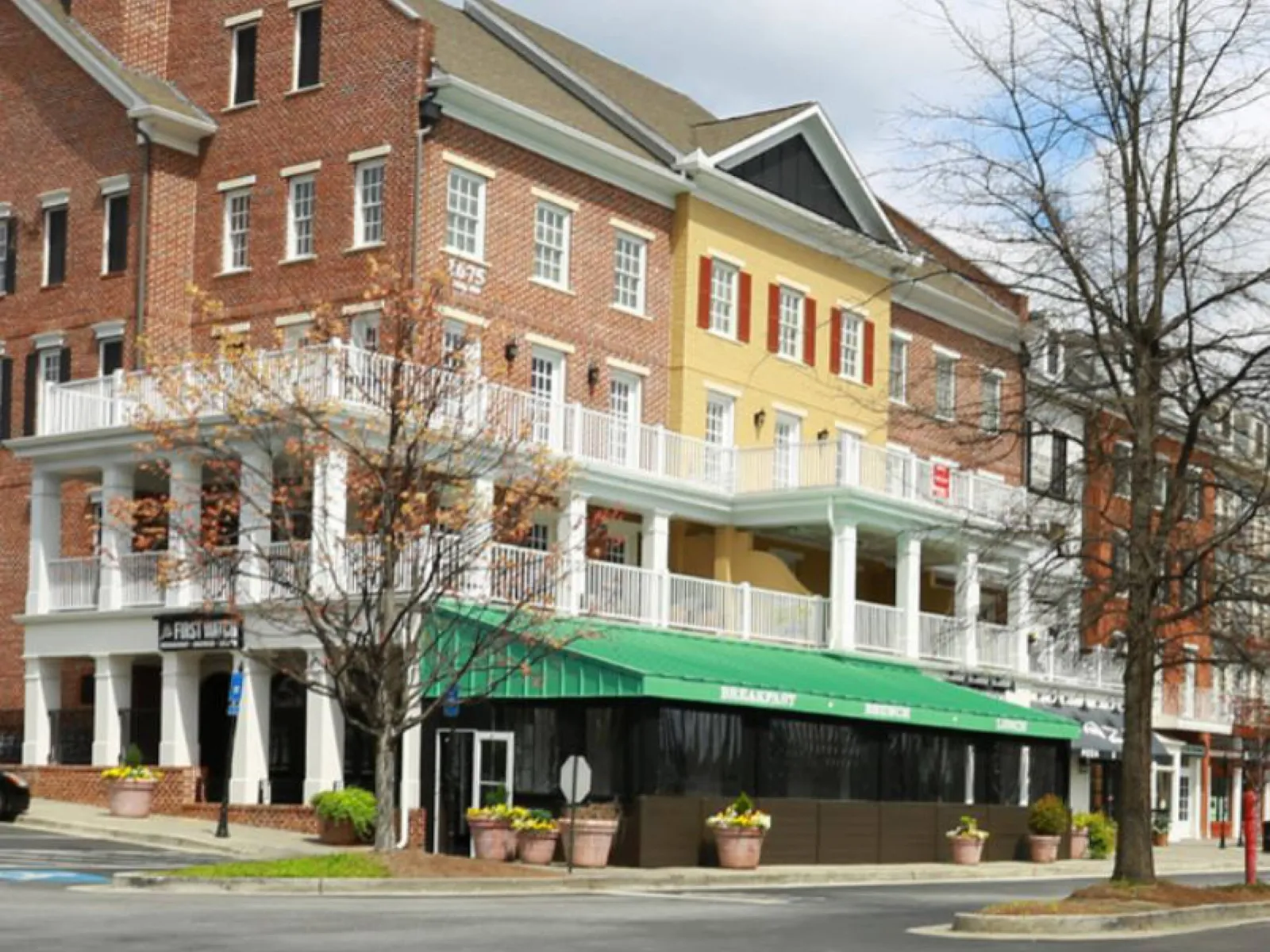 Three-story brick and yellow townhouses with white balconies and a ground floor cafe with a green awning on a street corner