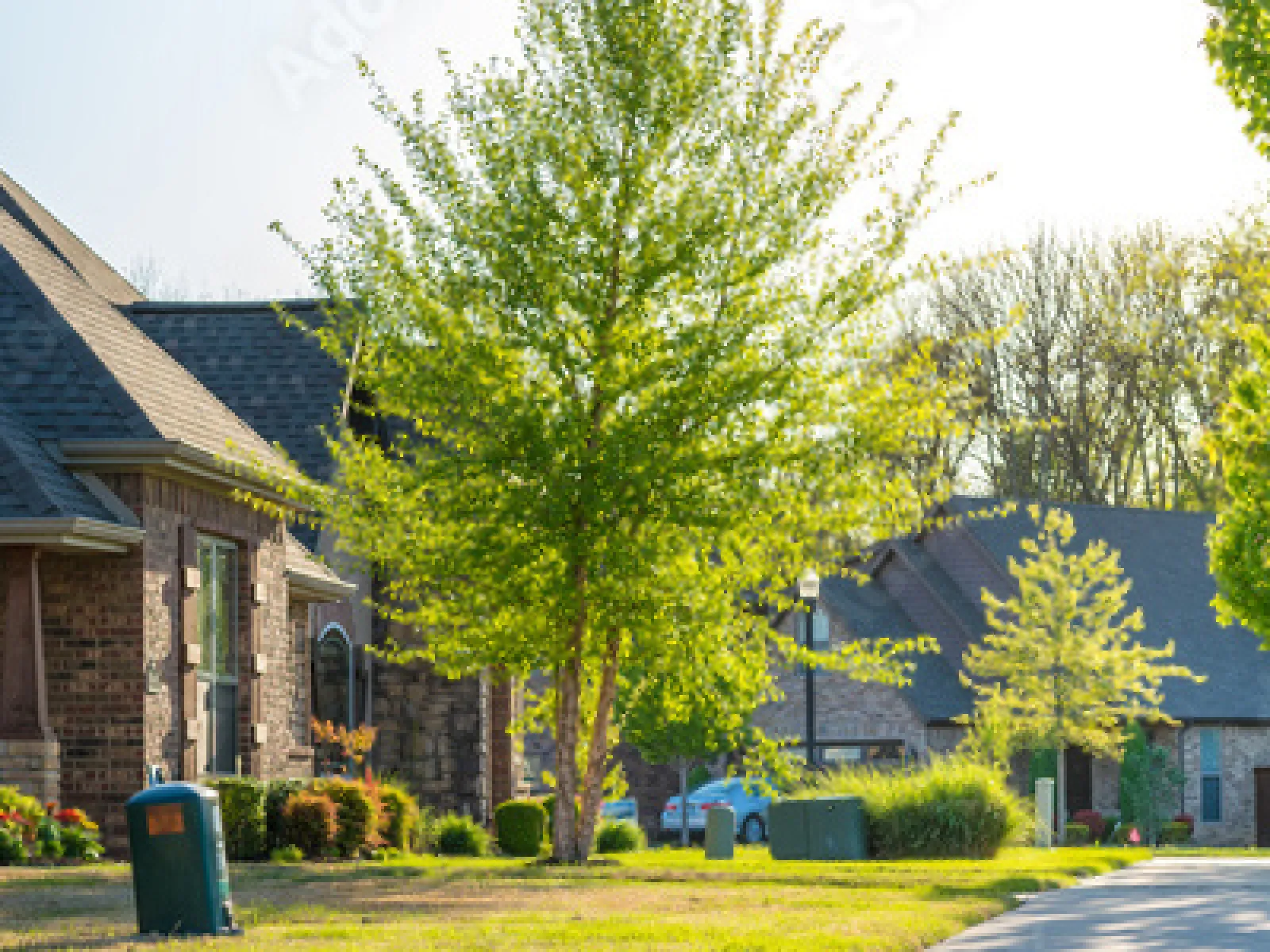 Suburban neighborhood with brick houses, green trees, and a sunny street in springtime.