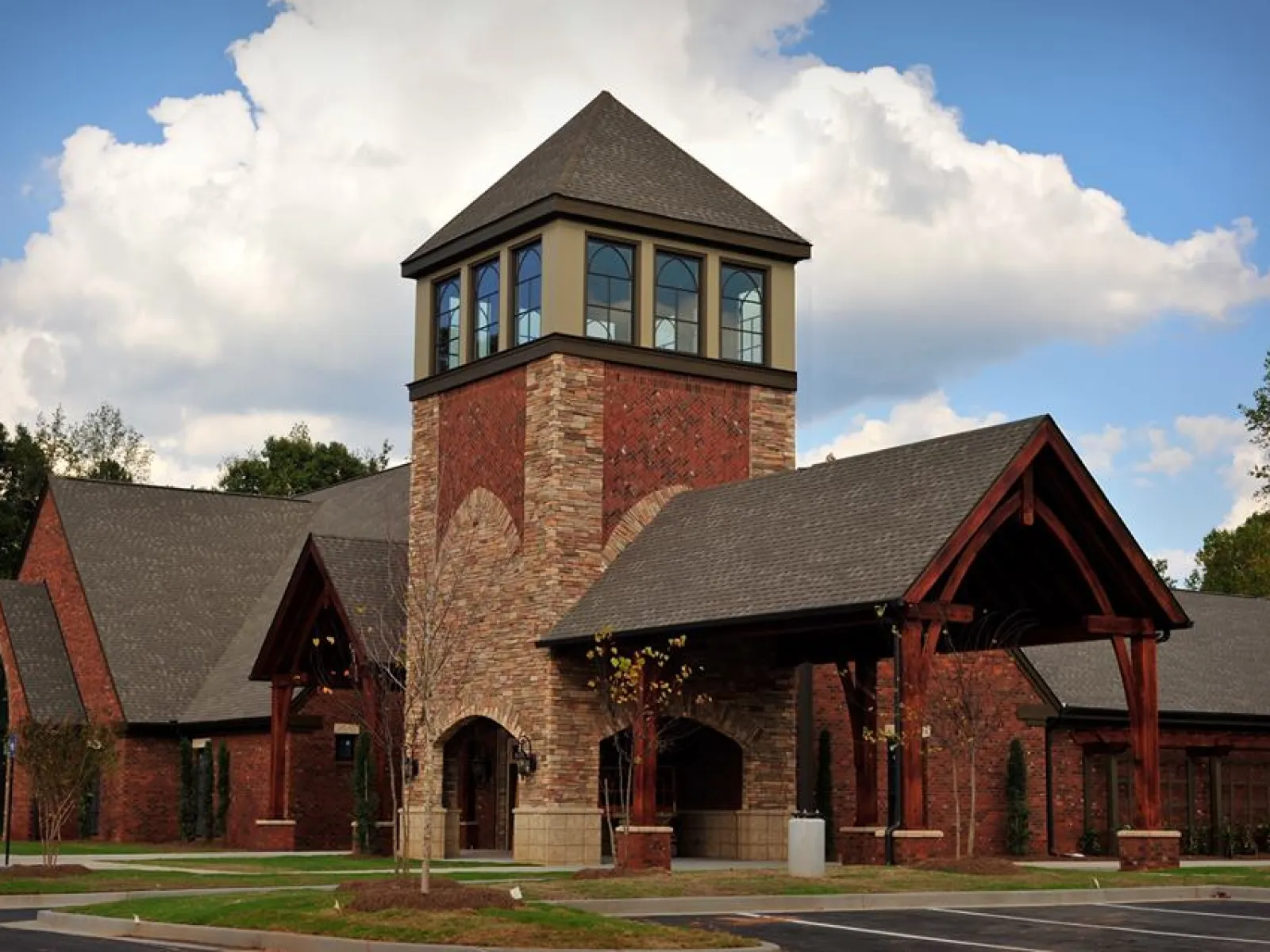 Brick building with stone tower and large windows under a partly cloudy sky with surrounding trees.
