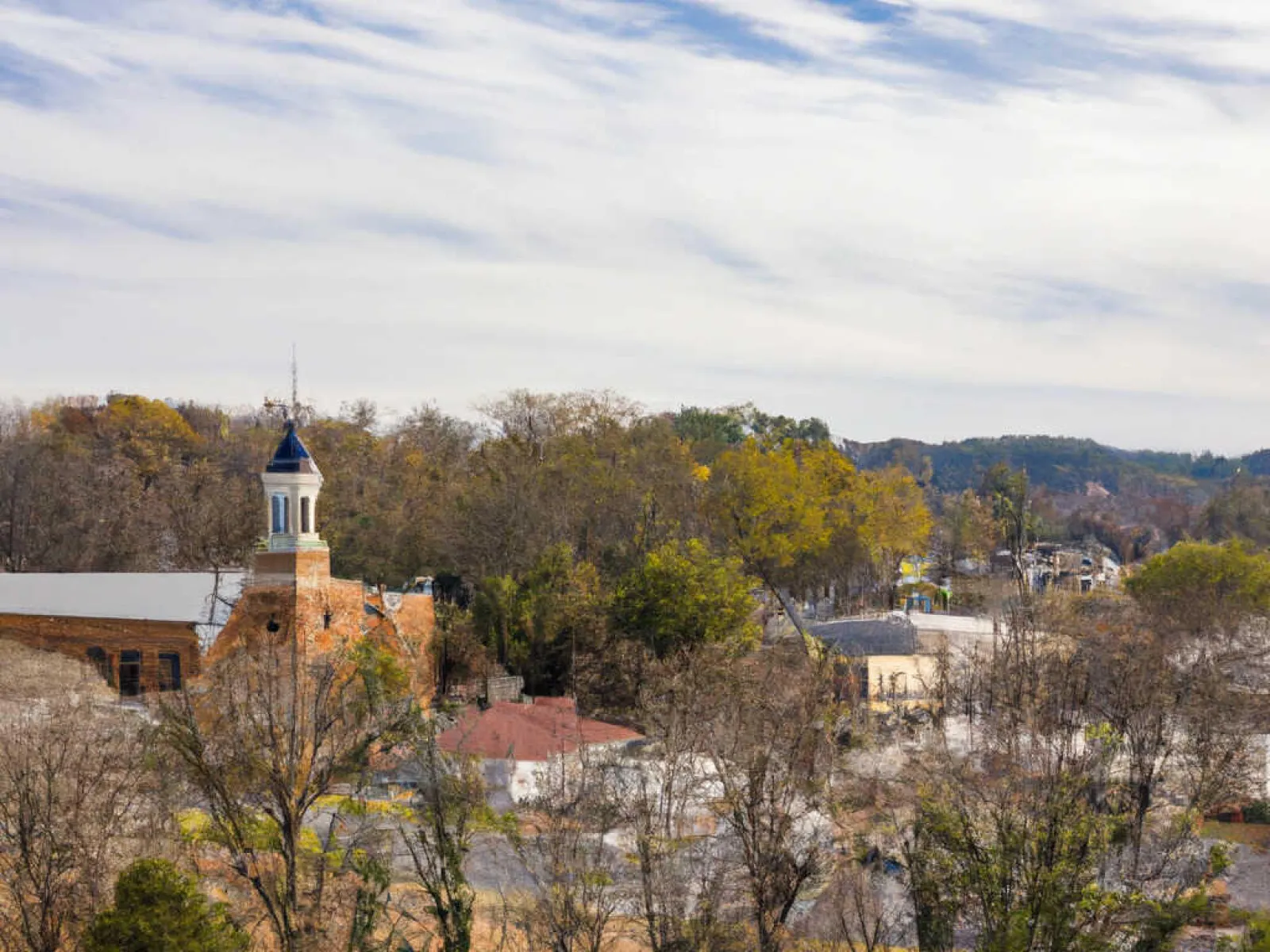 View of a small town with a historic brick building topped by a cupola amid autumn trees under a cloudy sky