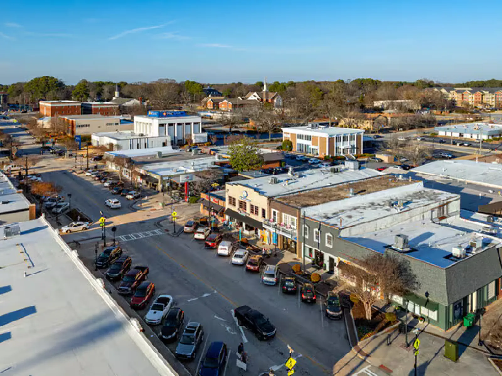 Aerial view of a busy small town main street with parked cars and low-rise commercial buildings on a clear day