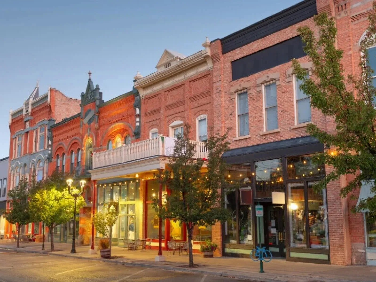 Historic downtown street with brick buildings, storefronts, trees, and evening lights on a calm sidewalk