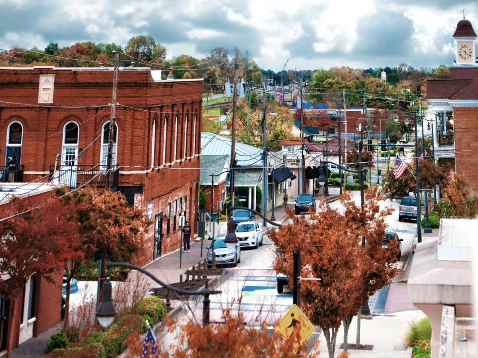Autumn view of a small town street with historic brick buildings, trees with fall foliage, and a clock tower under cloudy sky