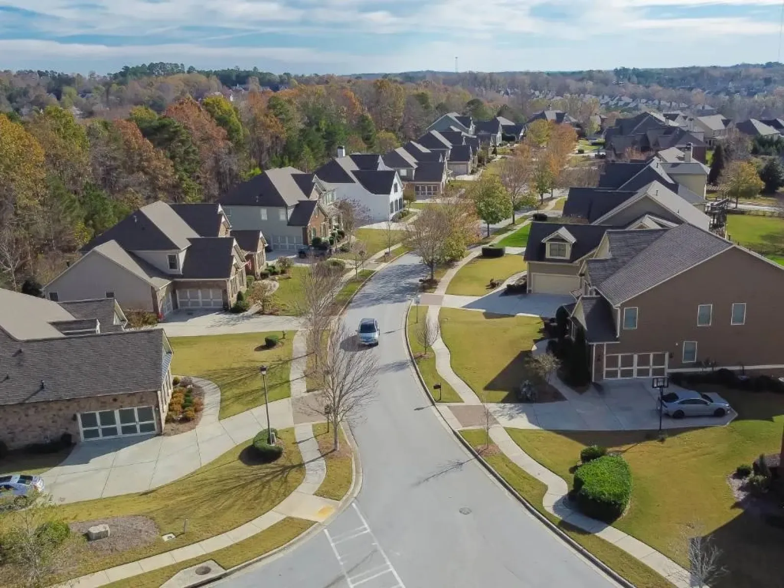Aerial view of a quiet suburban neighborhood with lined houses, curving roads, and trees in early autumn.