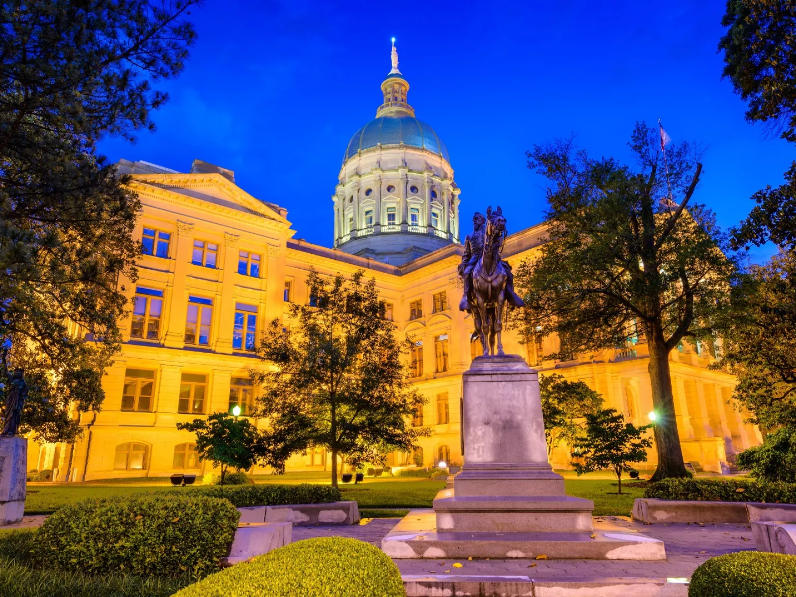 Georgia State Capitol building illuminated at dusk with equestrian statue and surrounding trees in foreground