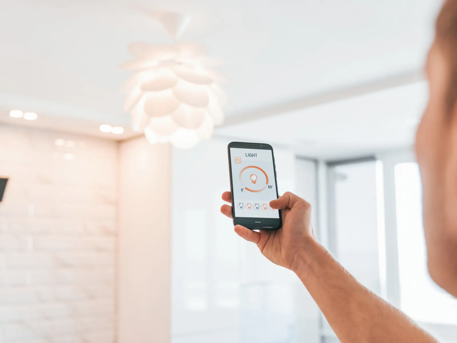Person controlling smart home lighting with a mobile app showing light brightness and color temperature settings.