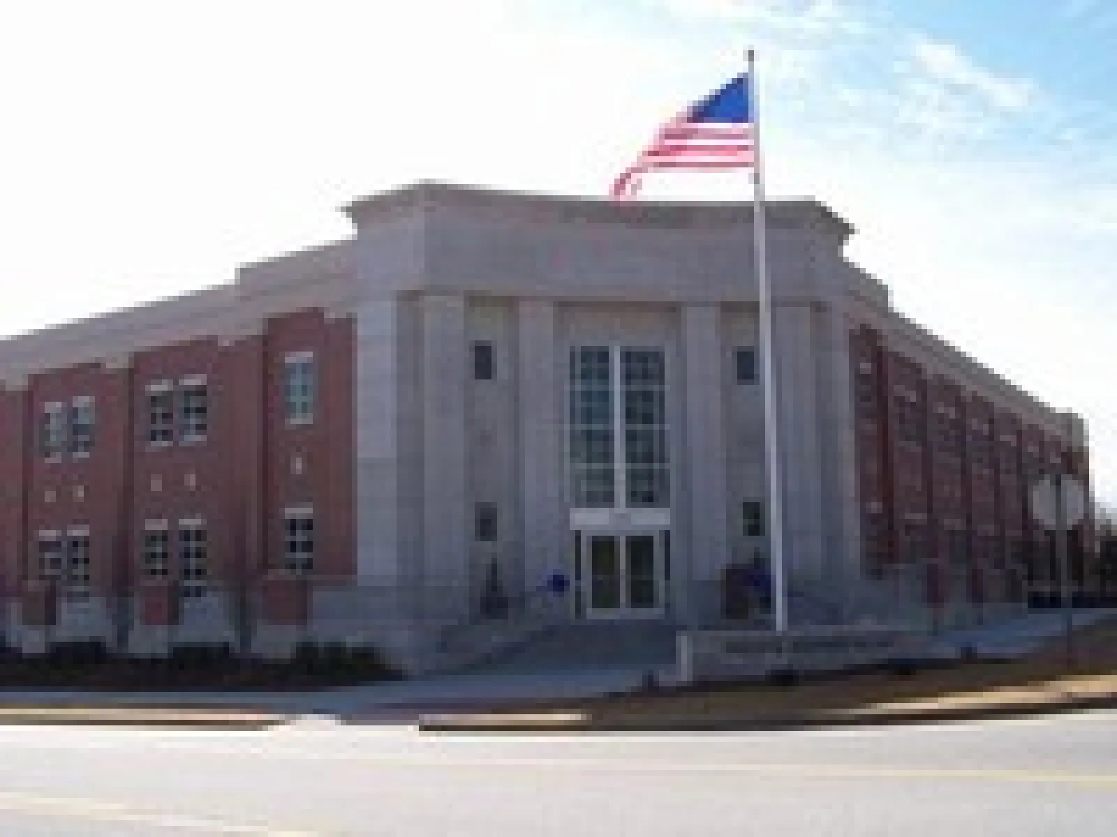 Large brick and stone government building with tall American flagpole in front under blue sky