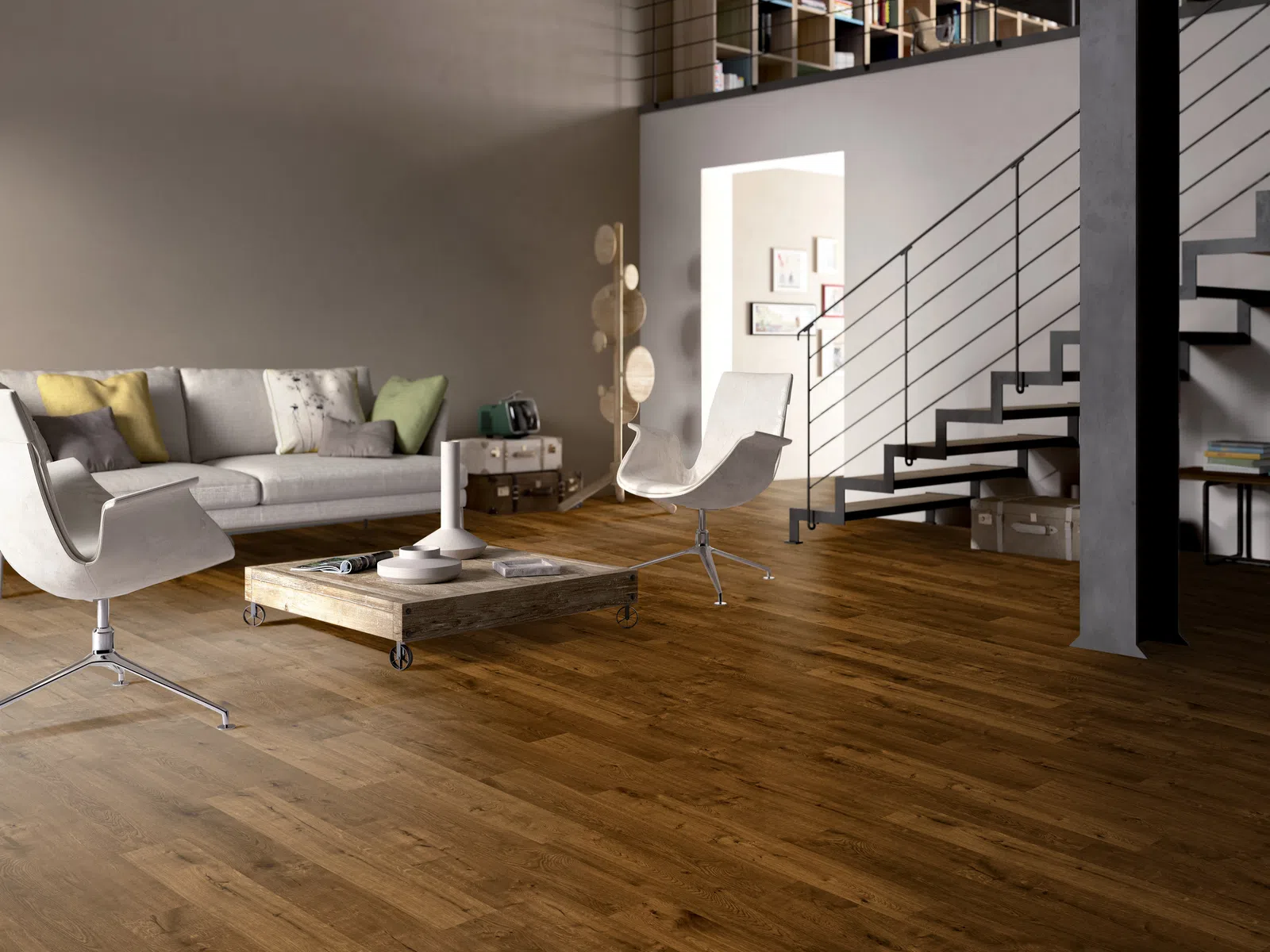 Modern living room with wooden floor, gray sofa, white chairs, coffee table, and staircase to loft.