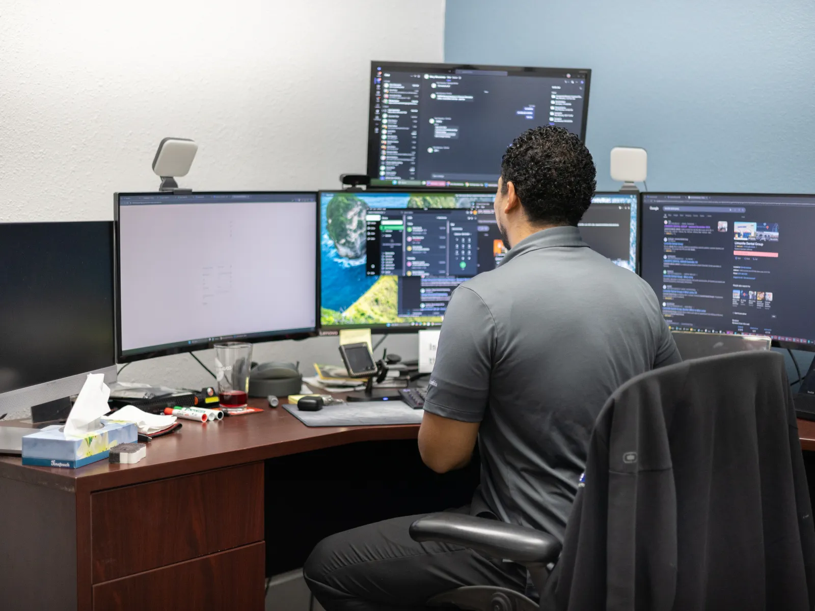 a man sitting at a desk with several monitors