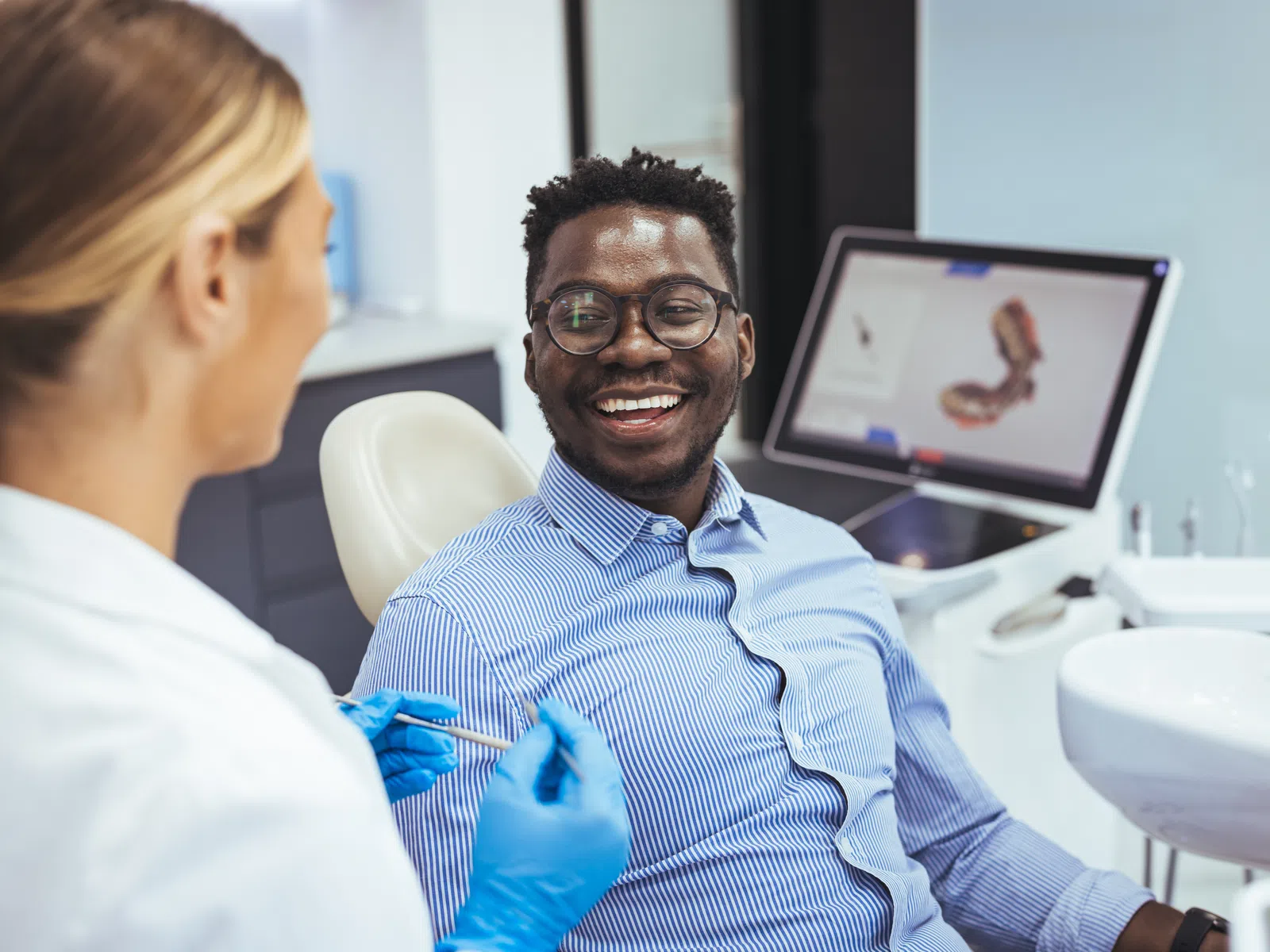 Dentist in blue gloves discusses dental care with smiling patient in modern clinic with dental equipment.