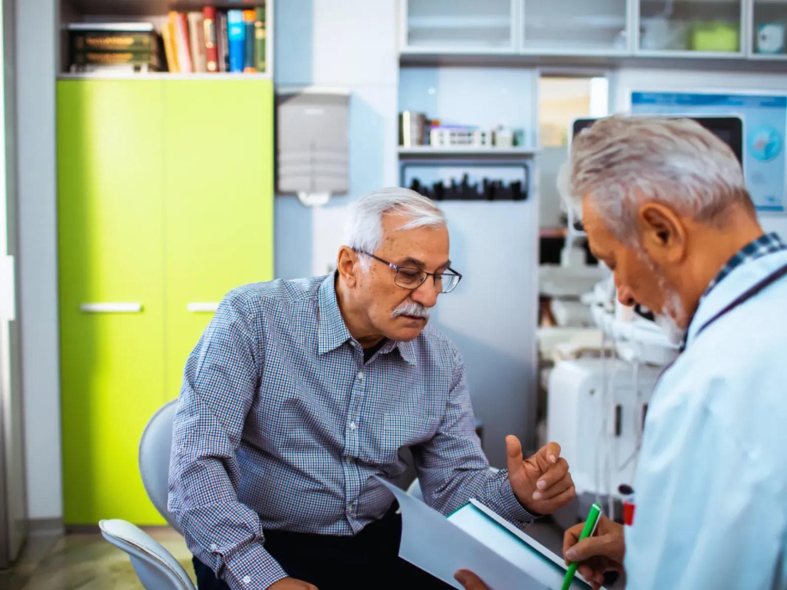 Elderly man consulting with a doctor in medical office discussing health documents during appointment.