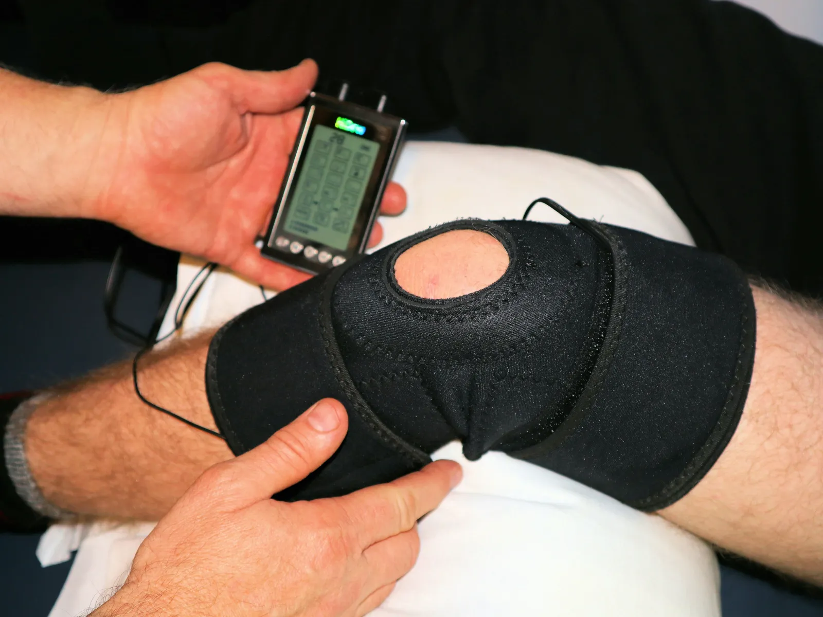 Therapeutic knee brace with electronic device applied for pain relief treatment on a person's leg.