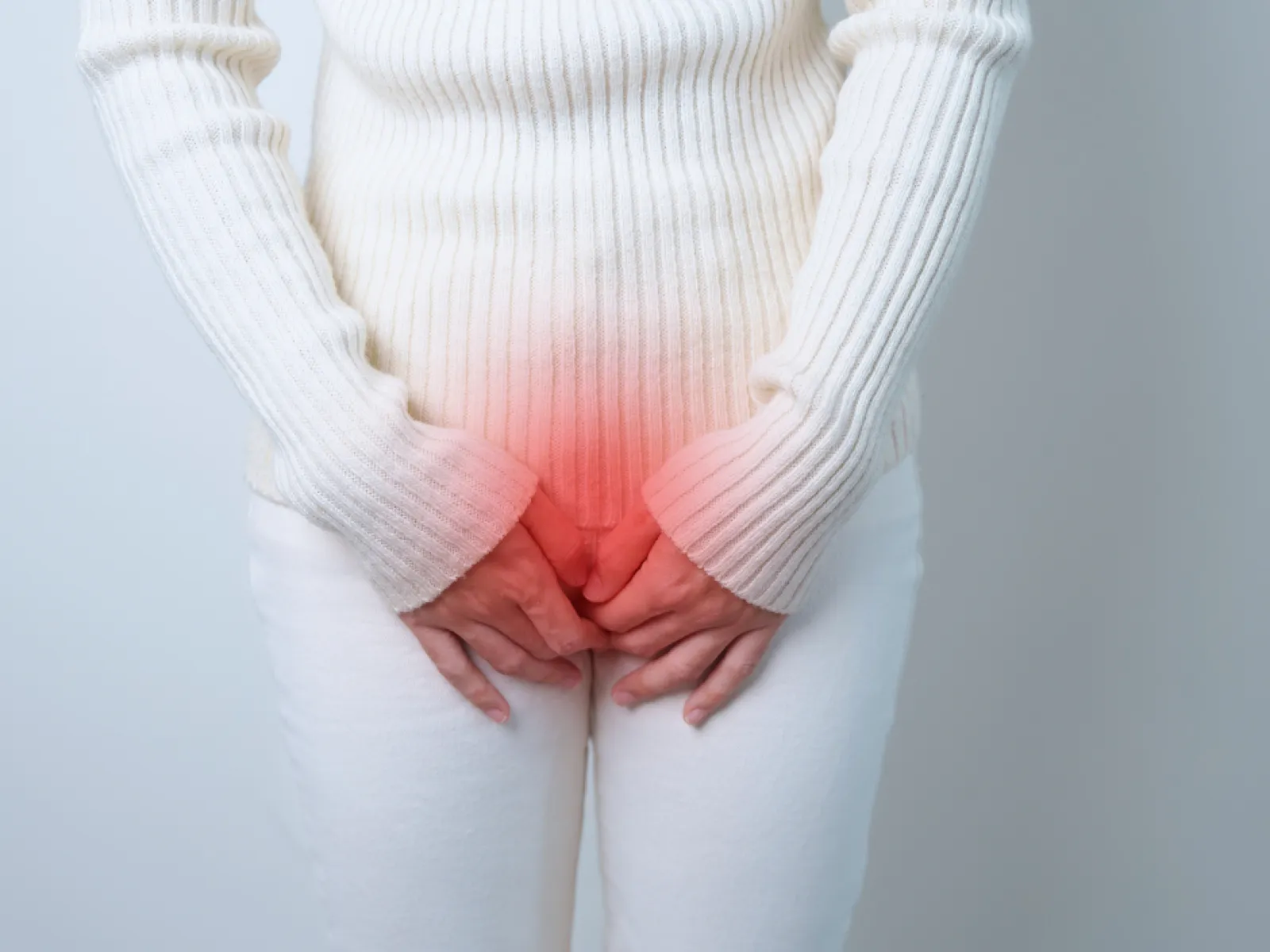 Person wearing white sweater and pants holding their lower abdomen with red highlight indicating pain or discomfort.