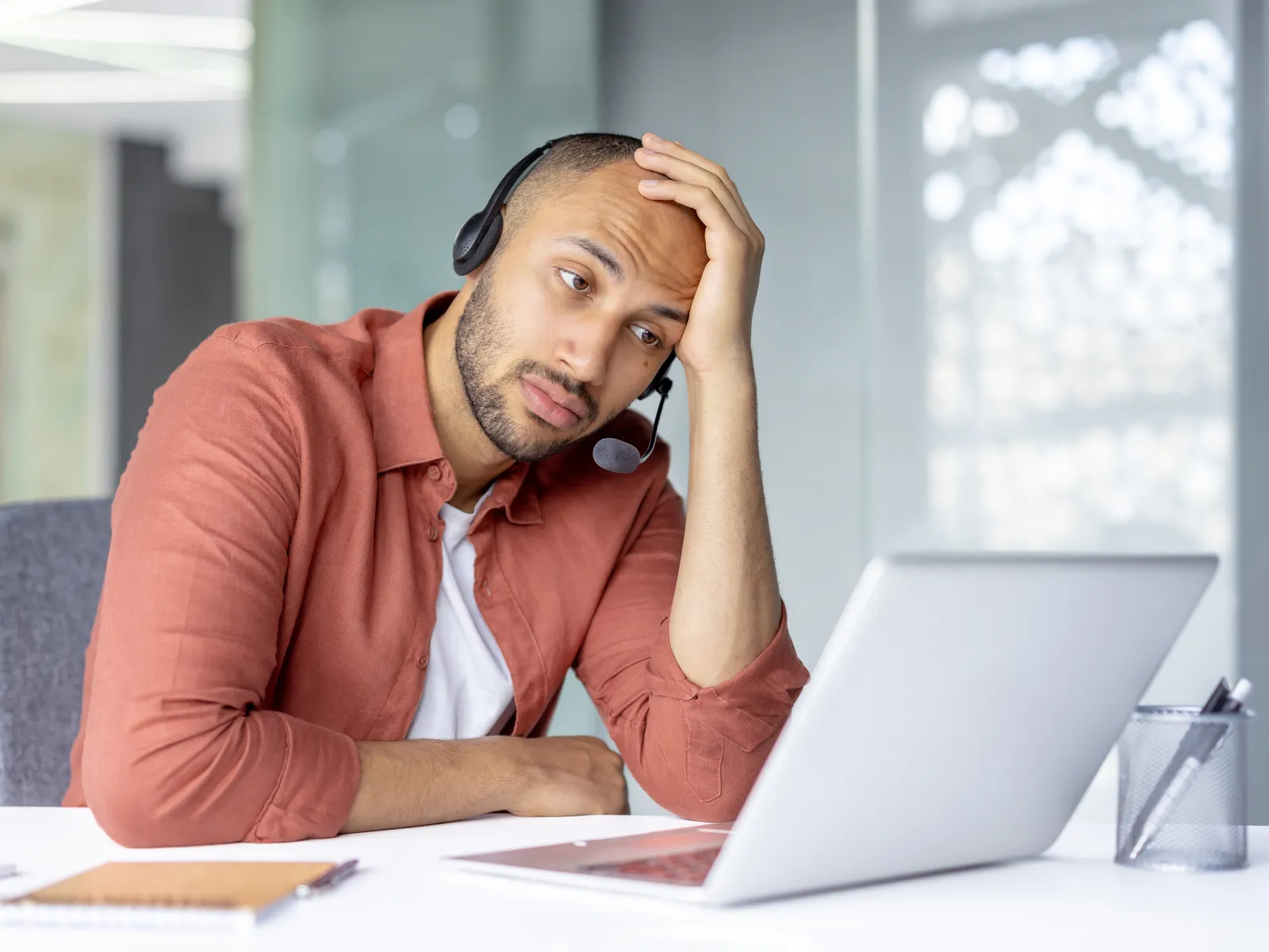 Tired man with headset looking stressed while working on laptop at office desk