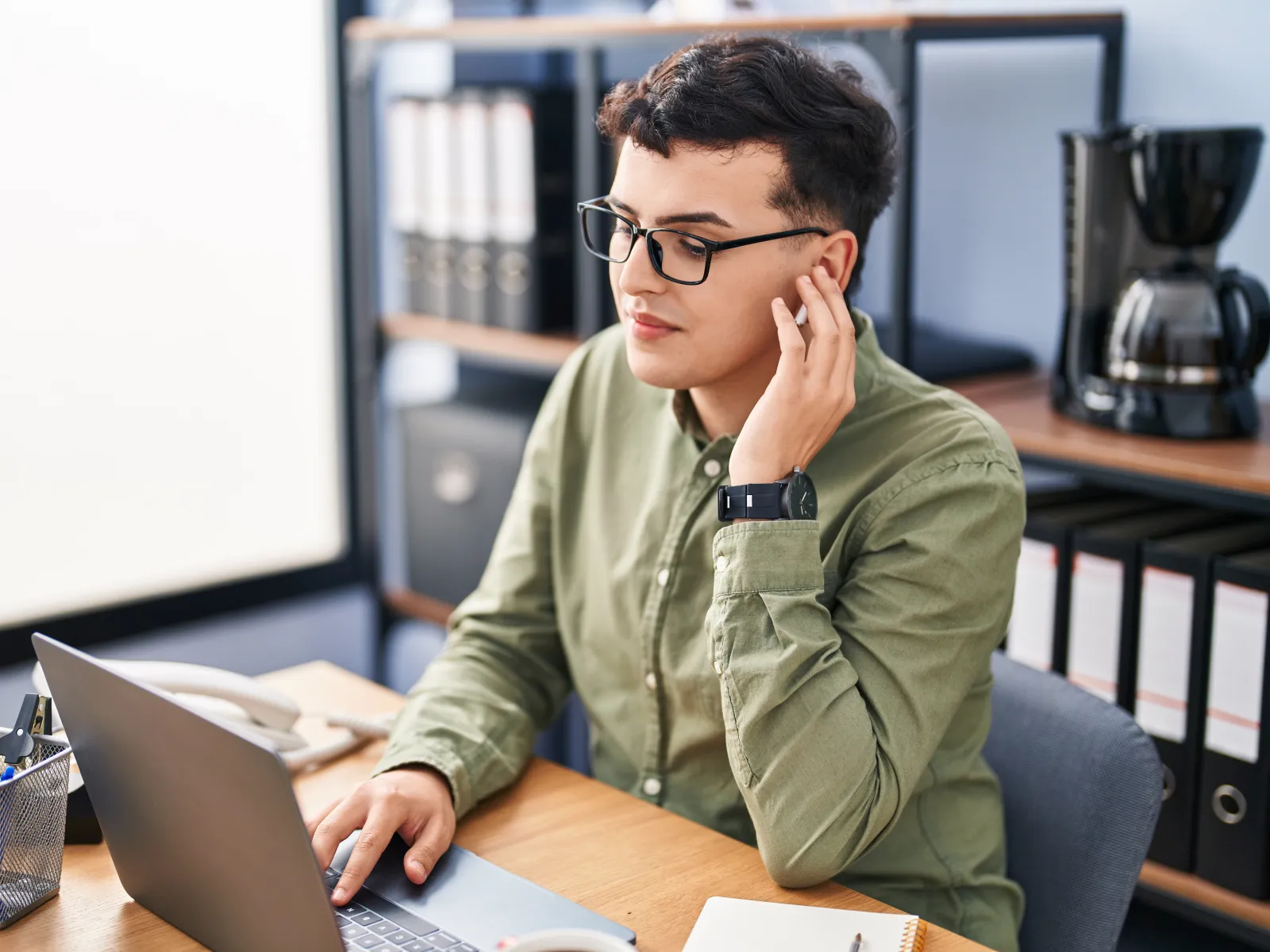Professional woman in glasses working on laptop with documents at wooden desk in modern office environment