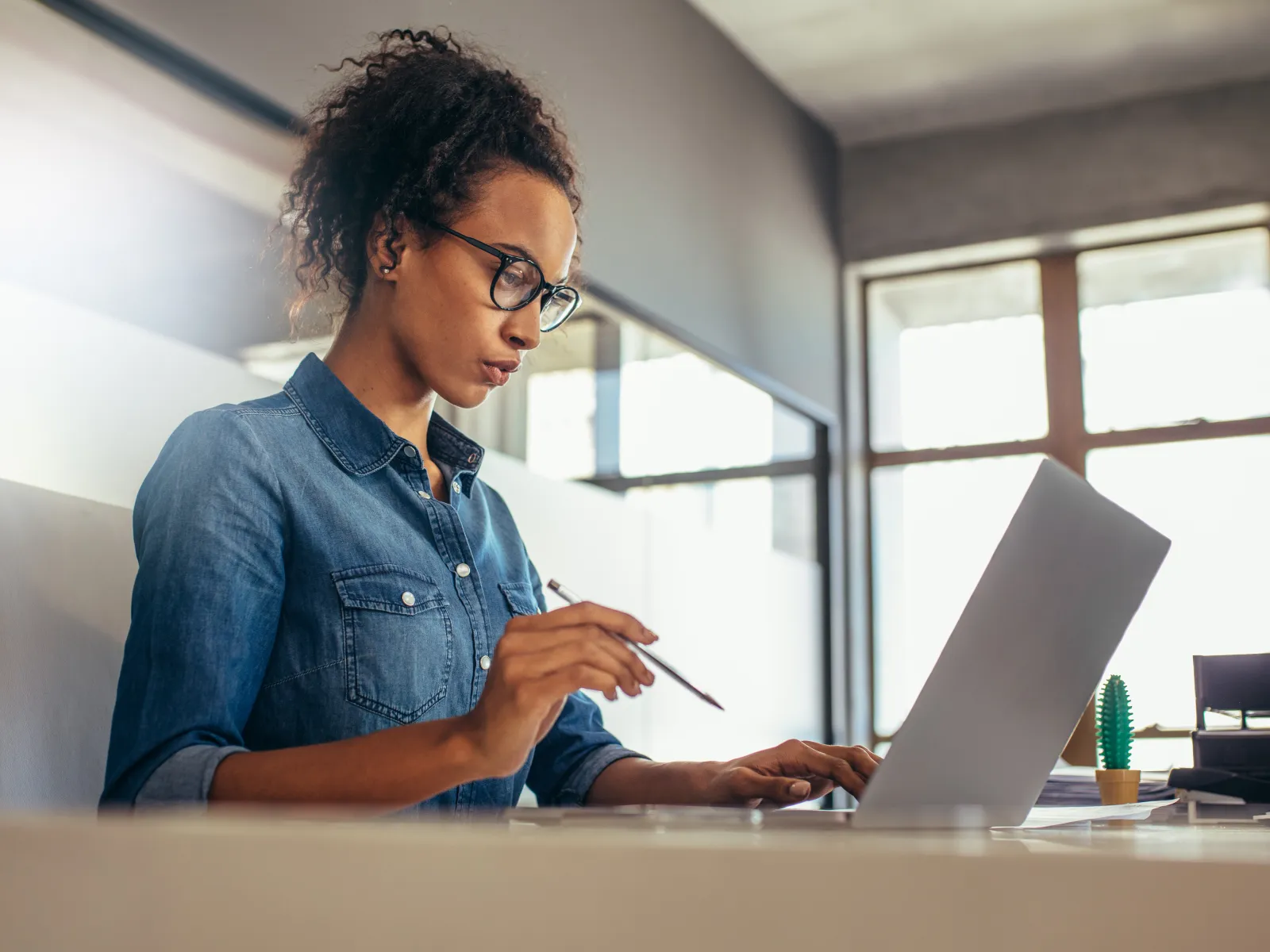 Man in blue shirt working at desk rubbing eyes looking stressed or tired with computer and papers around.