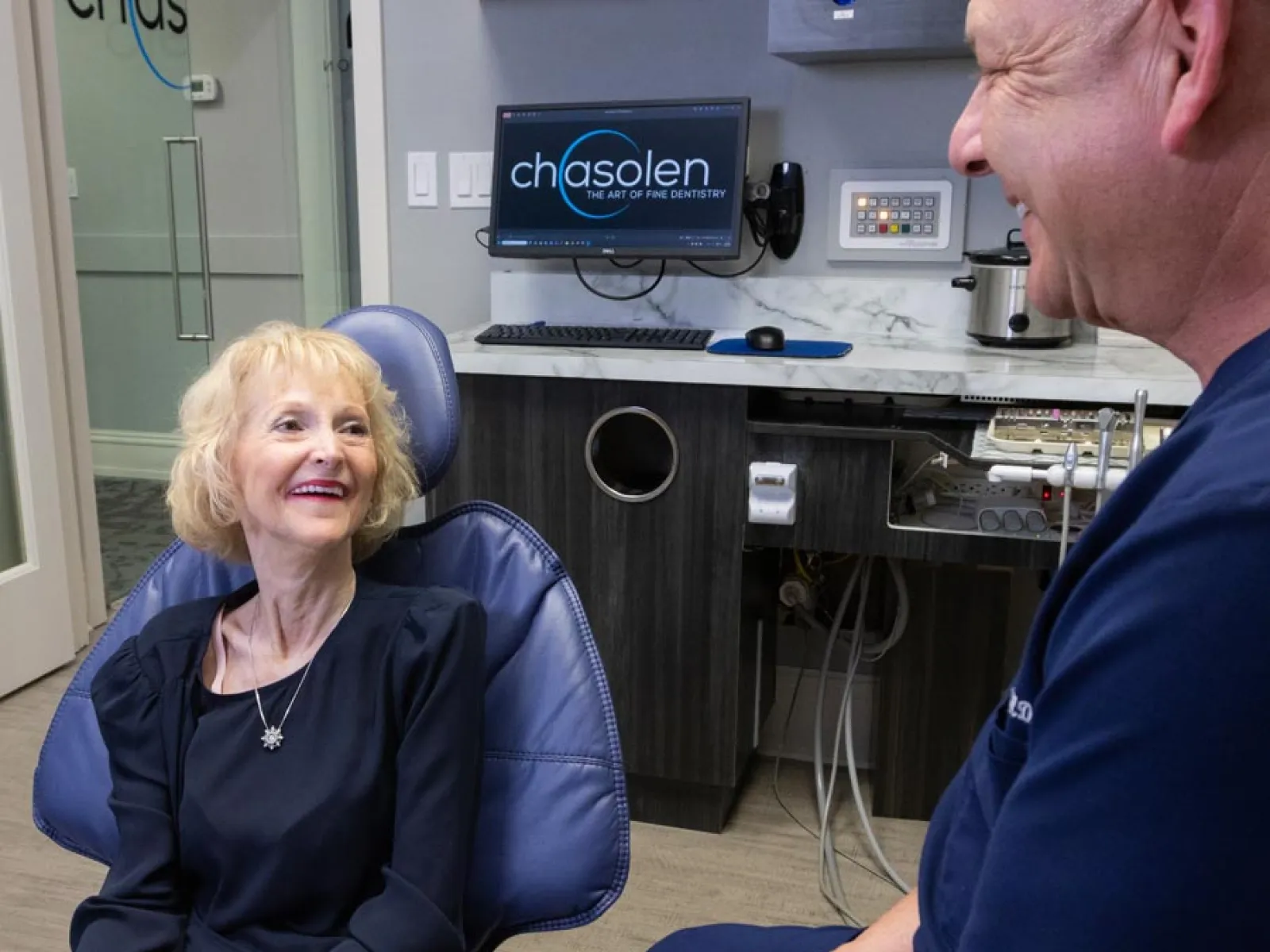 Smiling elderly woman in dental chair consulting with male dentist in modern dental office.