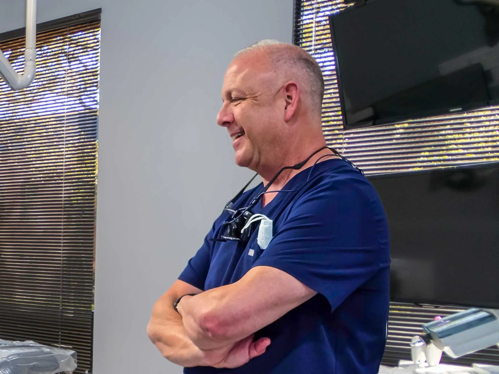 Smiling male healthcare professional in navy scrubs standing with arms crossed in medical office