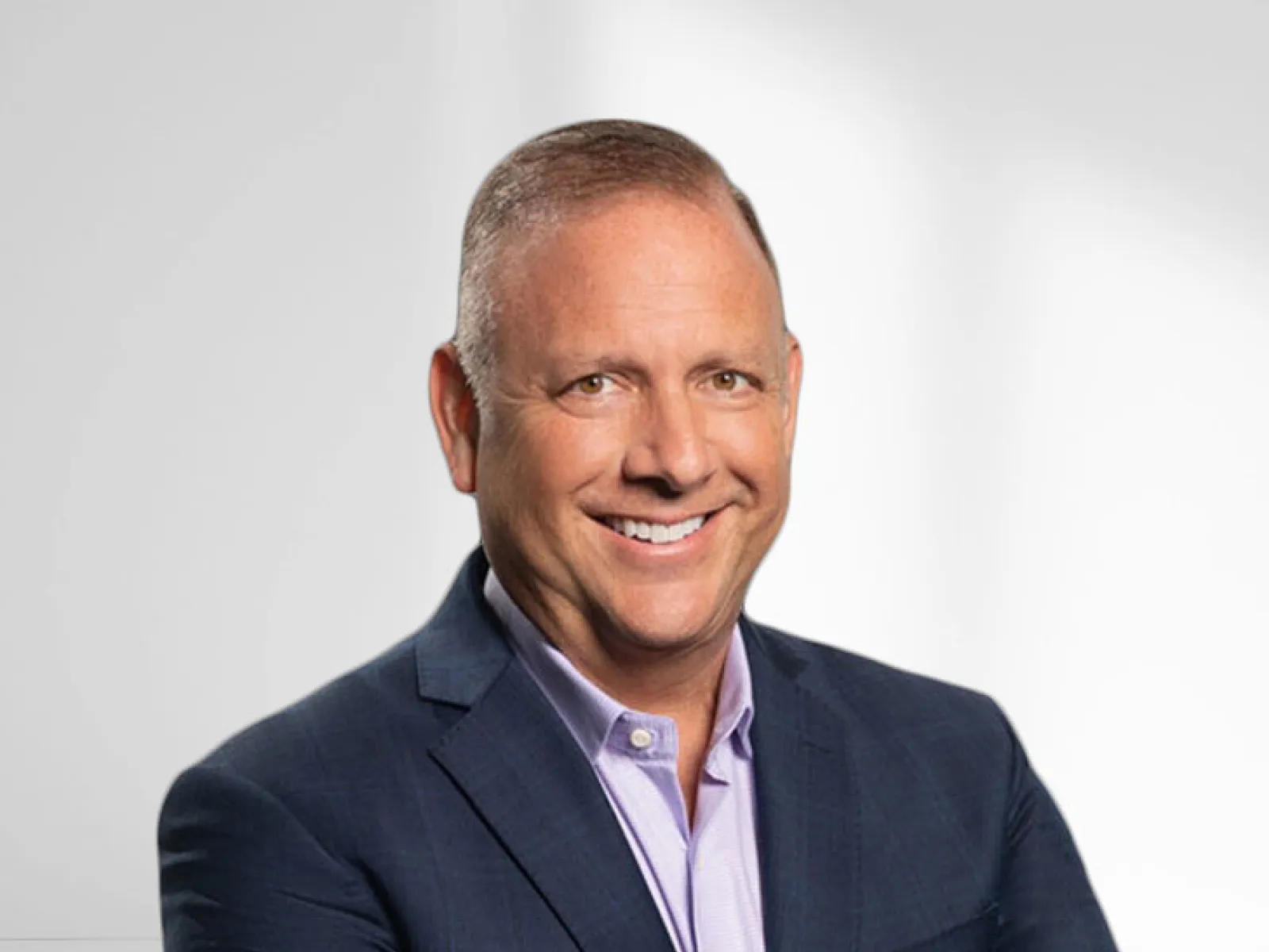 Smiling middle-aged man in a dark suit and light purple shirt against a plain light background