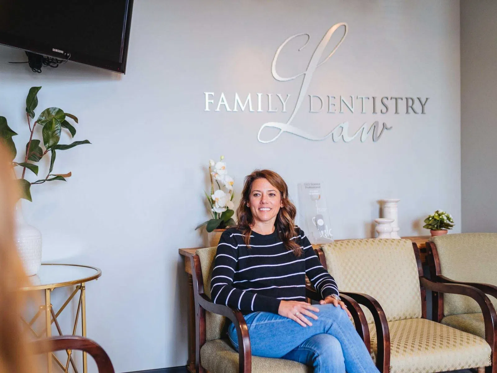 Woman in striped sweater sitting in dental office waiting room with Family Dentistry Law sign in background
