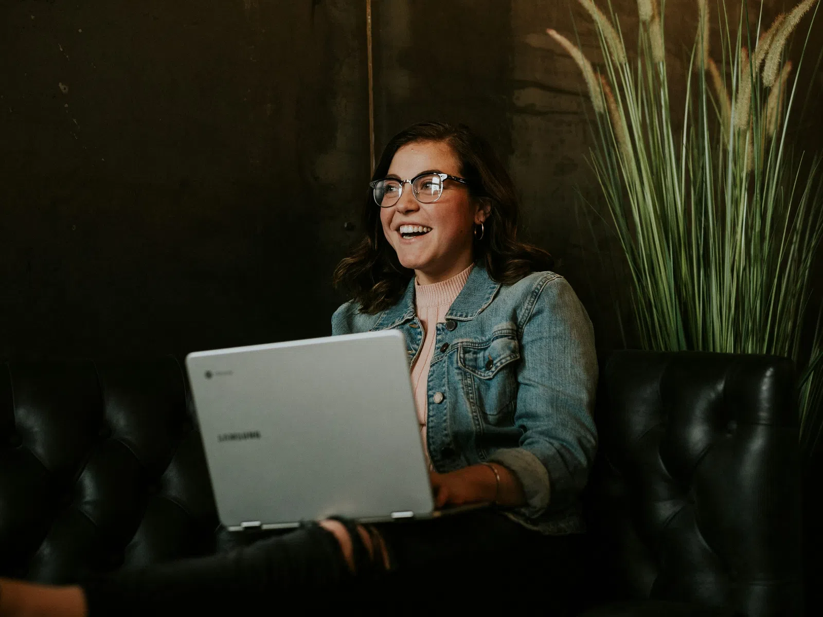 Smiling businessman wearing glasses sitting at desk using laptop in modern office with natural light.