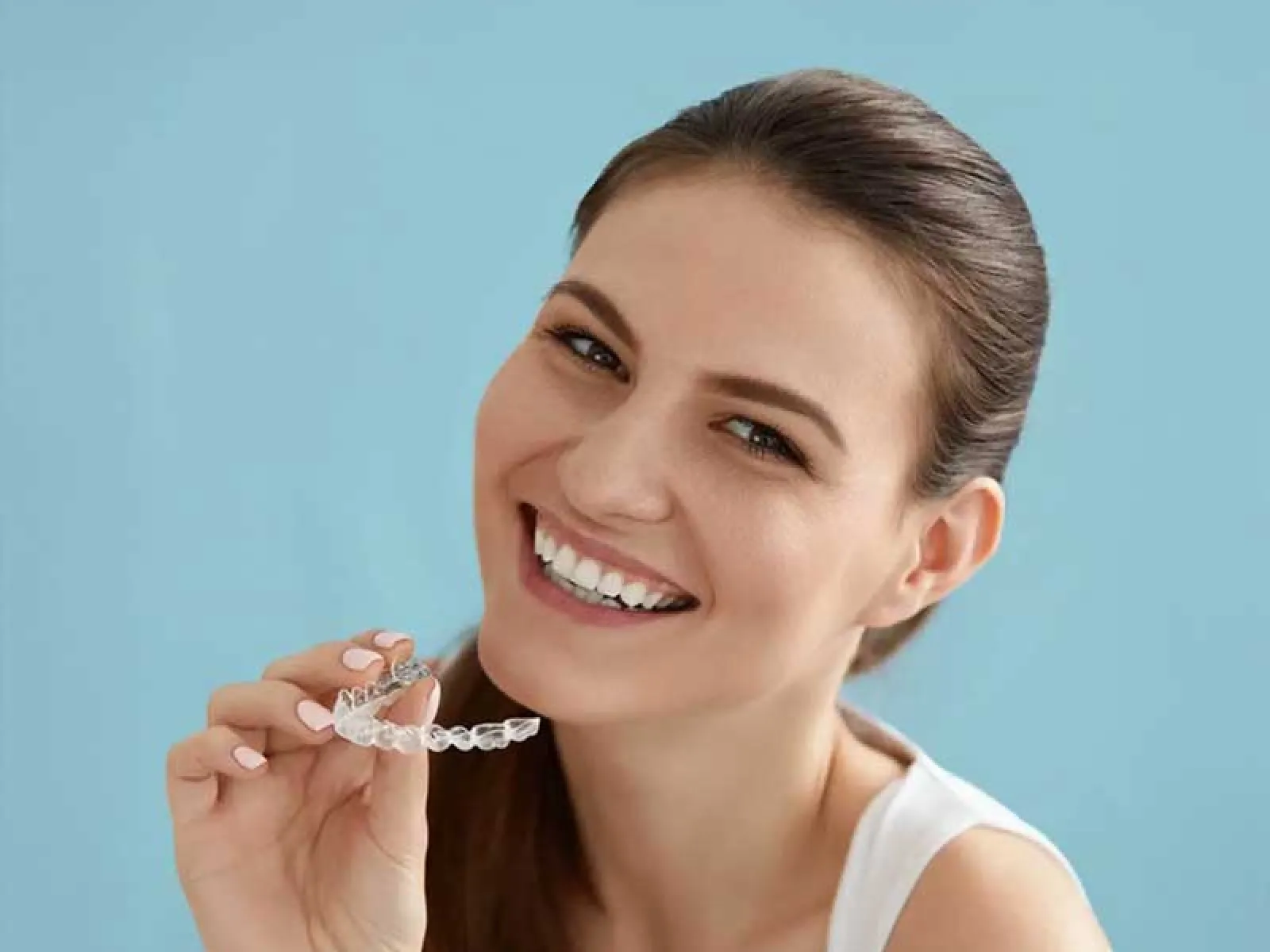 Smiling woman holding a clear dental aligner against a blue background, showcasing dental care and orthodontics.