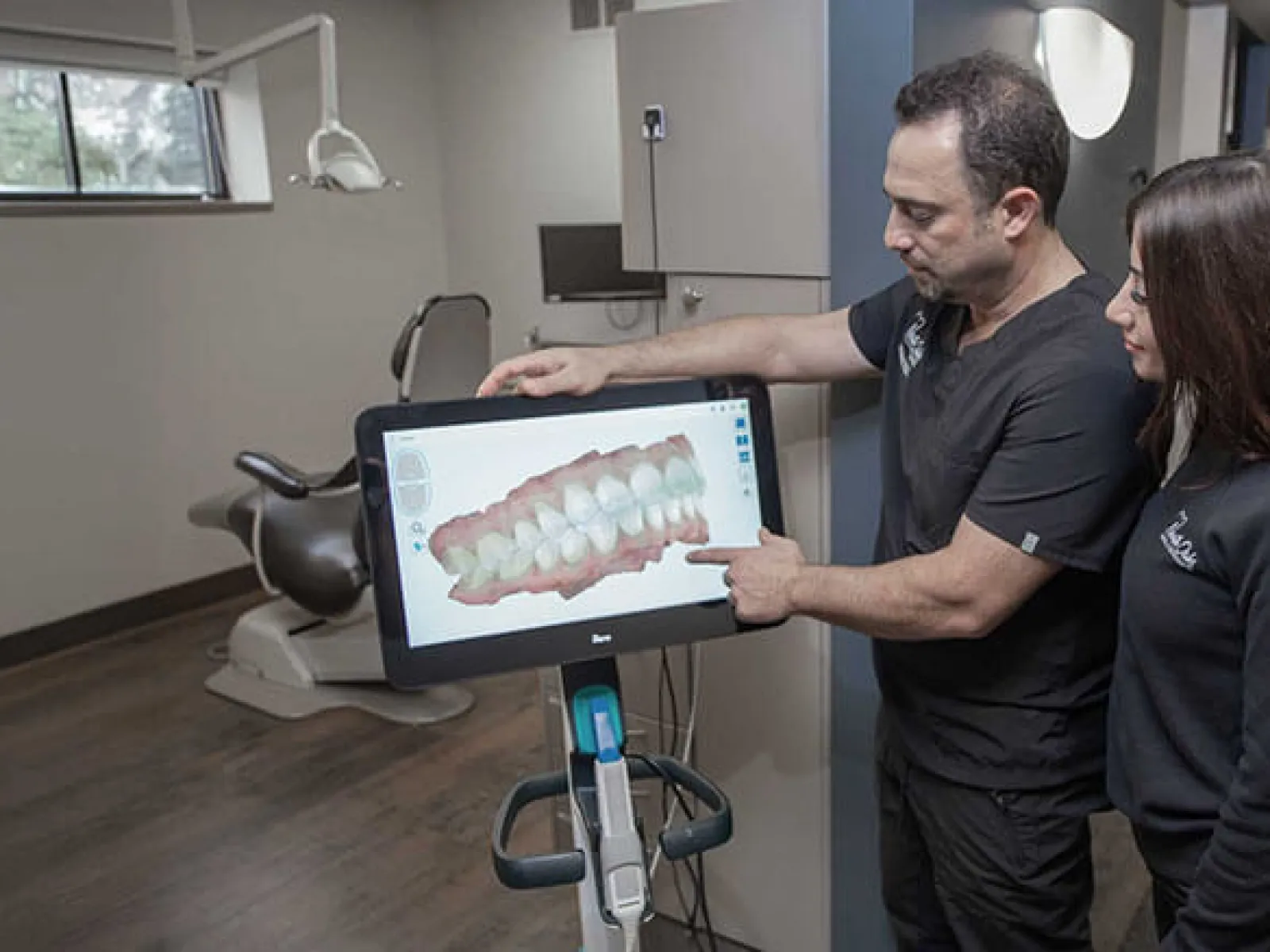Dentist showing dental 3D scan on screen to assistant in modern dental clinic room.