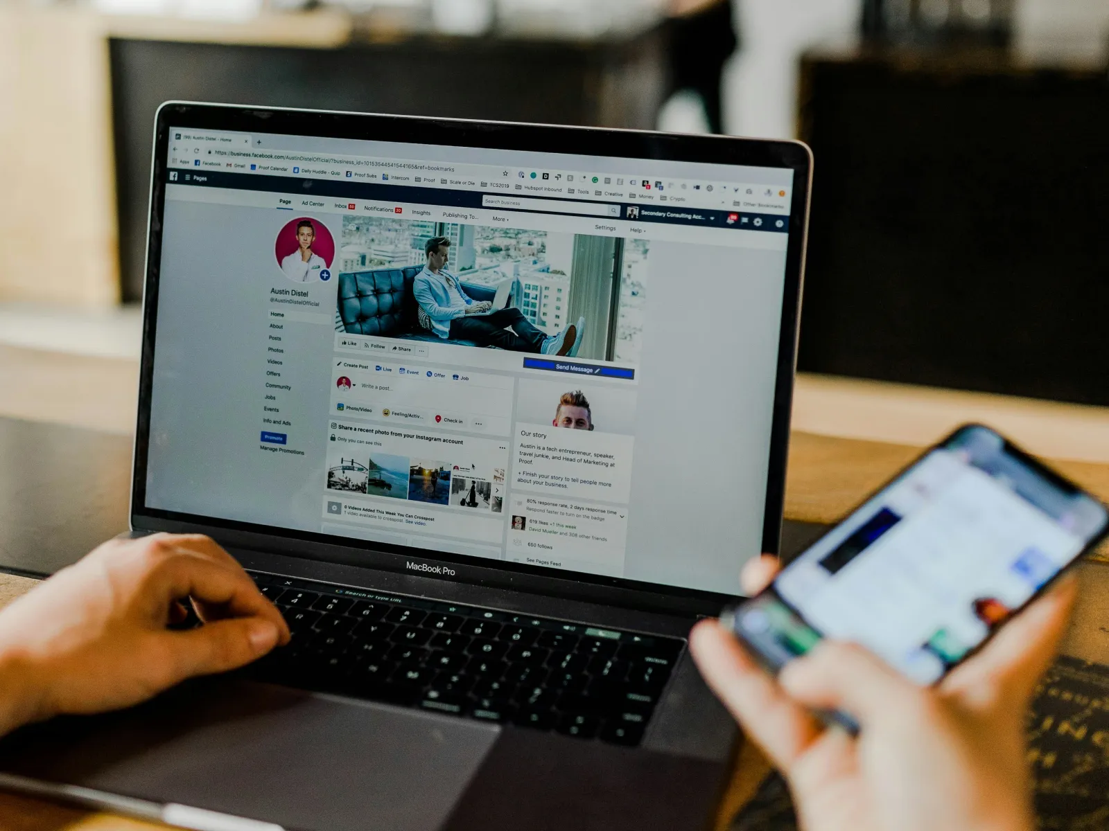 Person browsing social media on laptop and smartphone at a wooden desk with blurred background