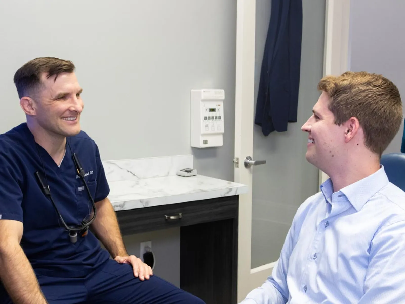 Dentist and patient smiling and talking during a consultation in a modern dental office room.