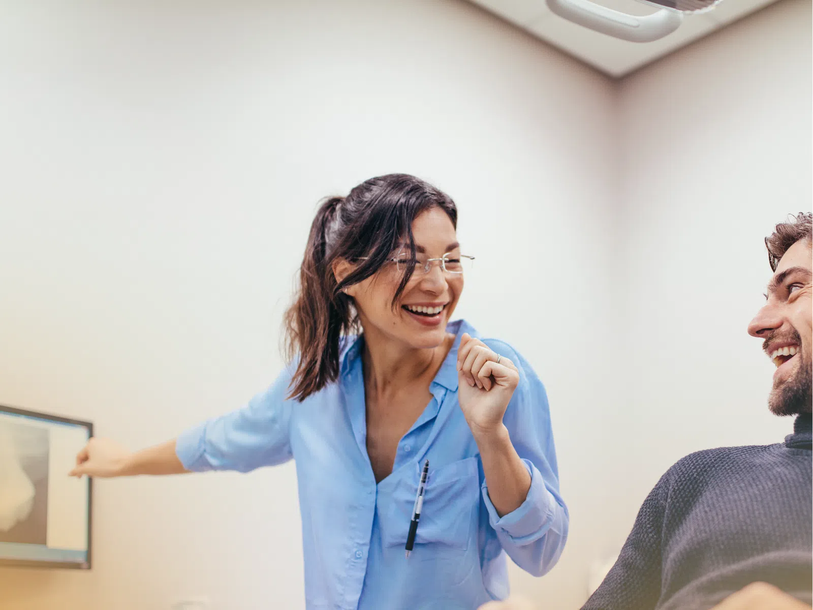 Smiling female dentist in blue shirt pointing at dental X-ray while patient in chair laughs