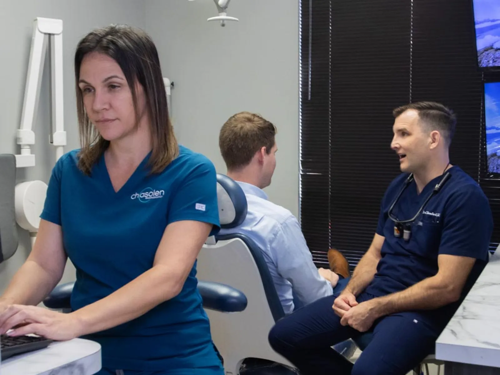 Dentist and assistant consulting a patient in a modern dental office with computer and equipment visible