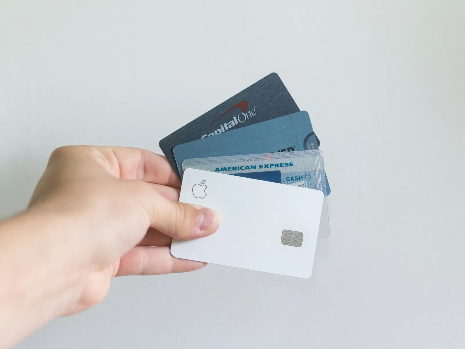 Hand holding Apple, Capital One, and American Express credit cards against a plain background.