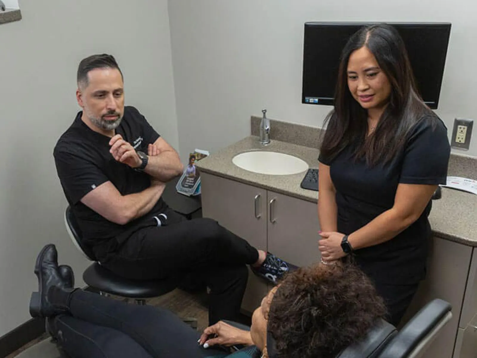 Patient reclining in a dental chair with two dental professionals consulting in a modern clinic room.