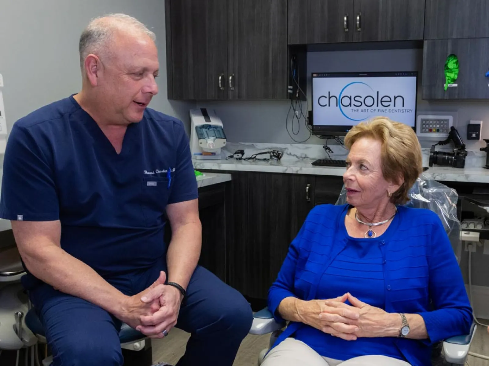Dentist consulting with senior woman patient in modern dental office with Chasolen sign in background